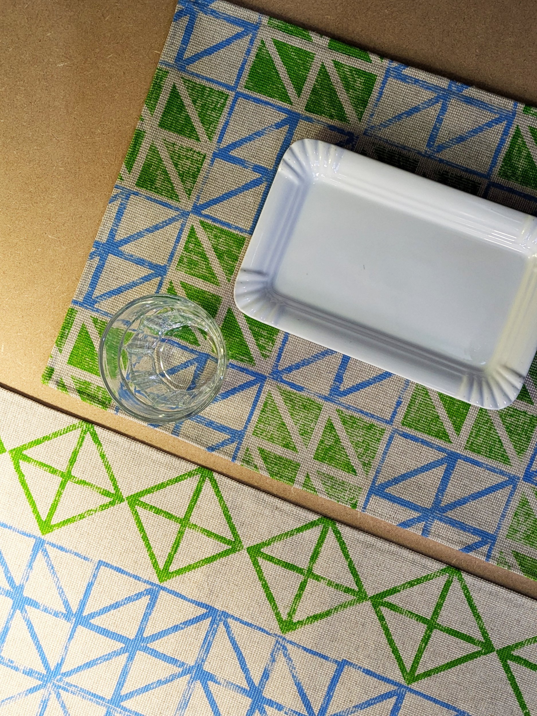 bright printed table runner and place mat next to each other on moody lit-up studio table scene