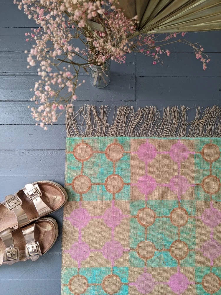geometric pattern in pastel colours on rug on floor with rose gold sandals and flower arrangement