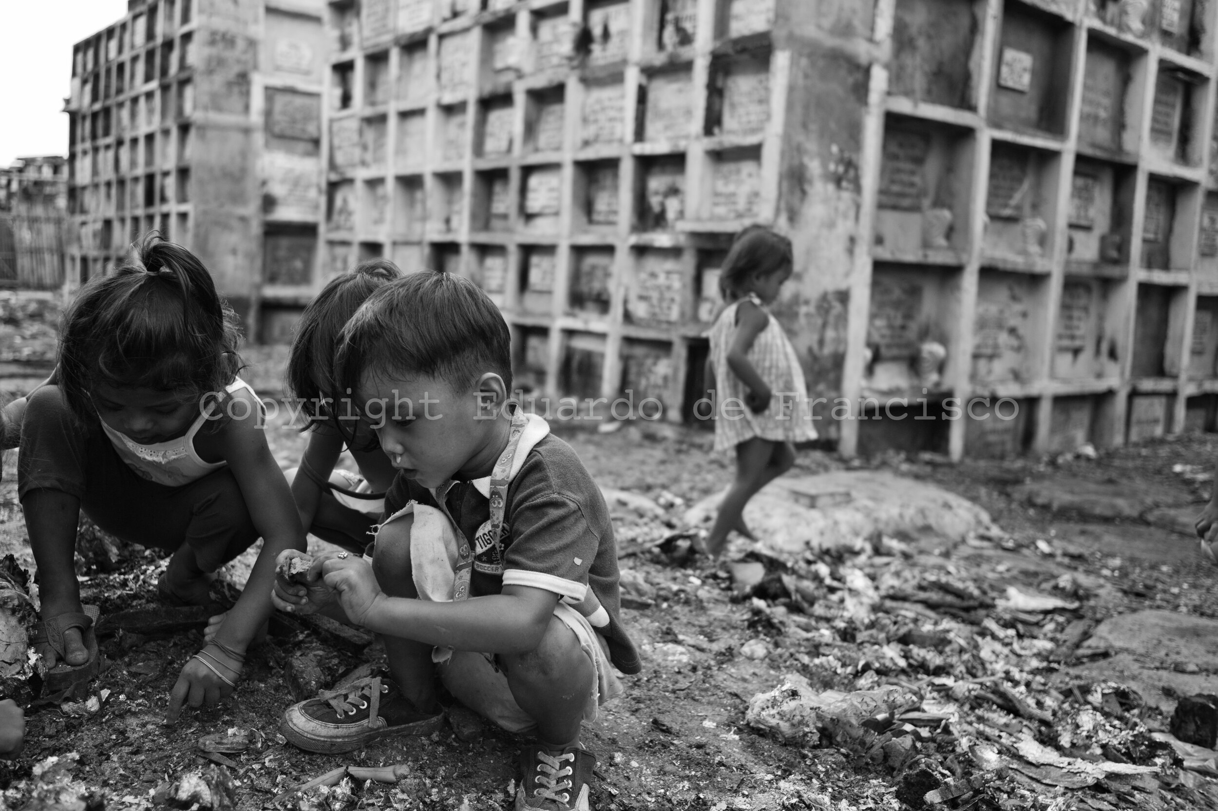  Navotas Cemetery, north of Tondo. A group of children, who live inside the cemetery with their families, search among the rests of burn waste for anything that can be reused. 