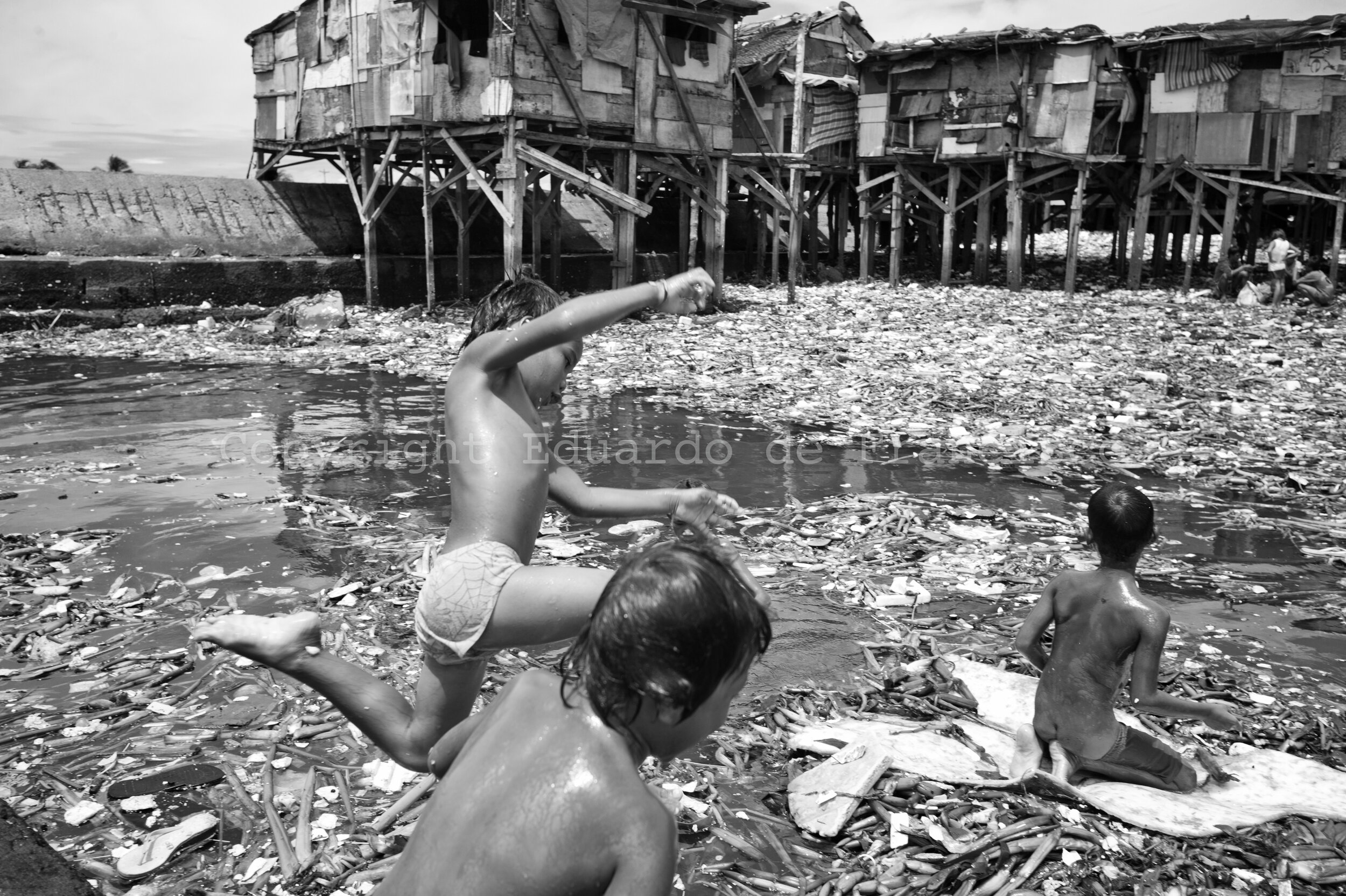 Children playing near the mouth of the Vitas river, which carries big amounts of rubbish and organic refuse into the see. 