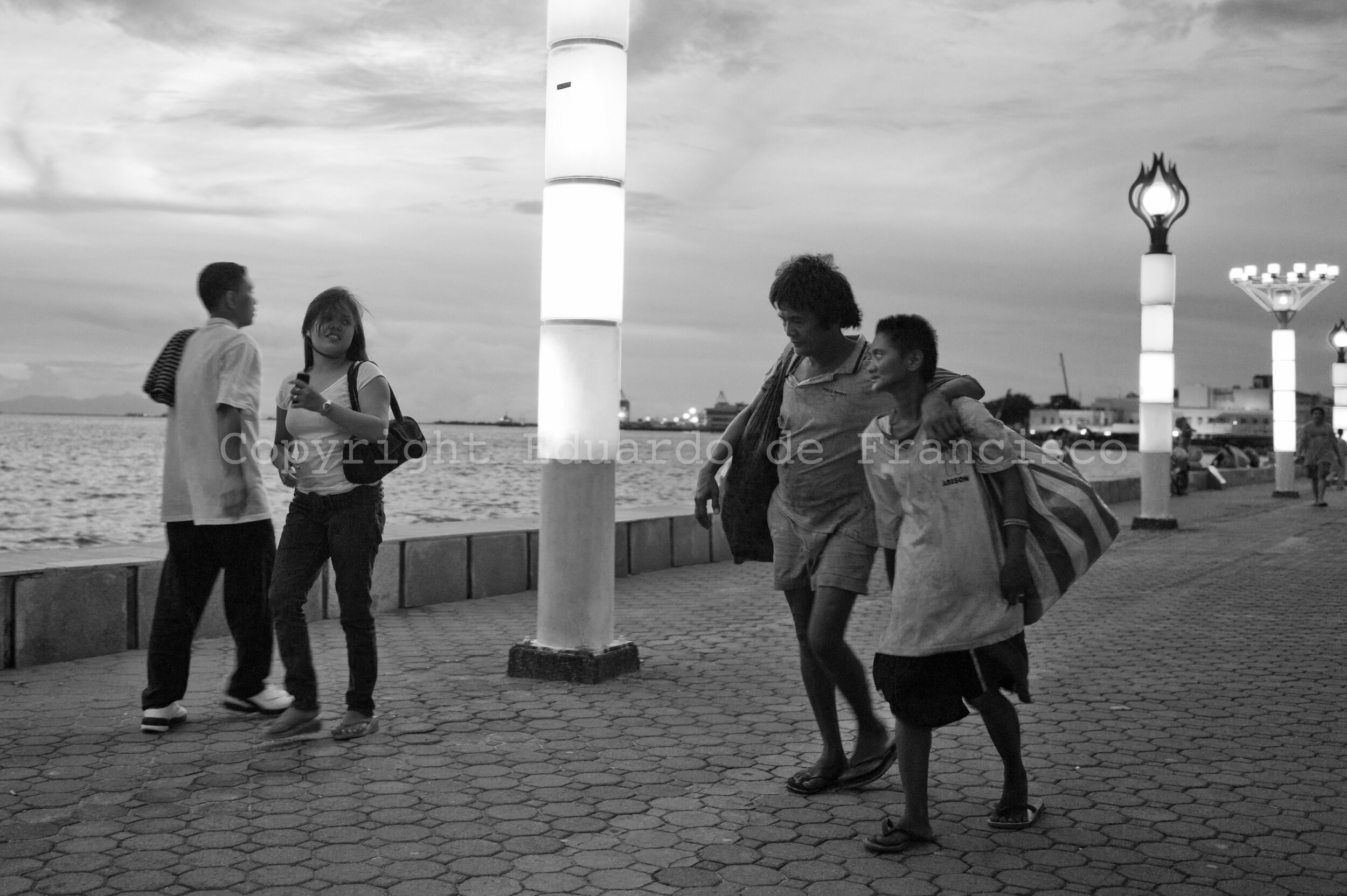  At dusk at Roxas Bulevard, two scavengers rummaging through the litter bins walk along middle-class Filipinos. They are very often invisible to these, who sometimes don't even know that, in the same city, thousands of families make a living from the