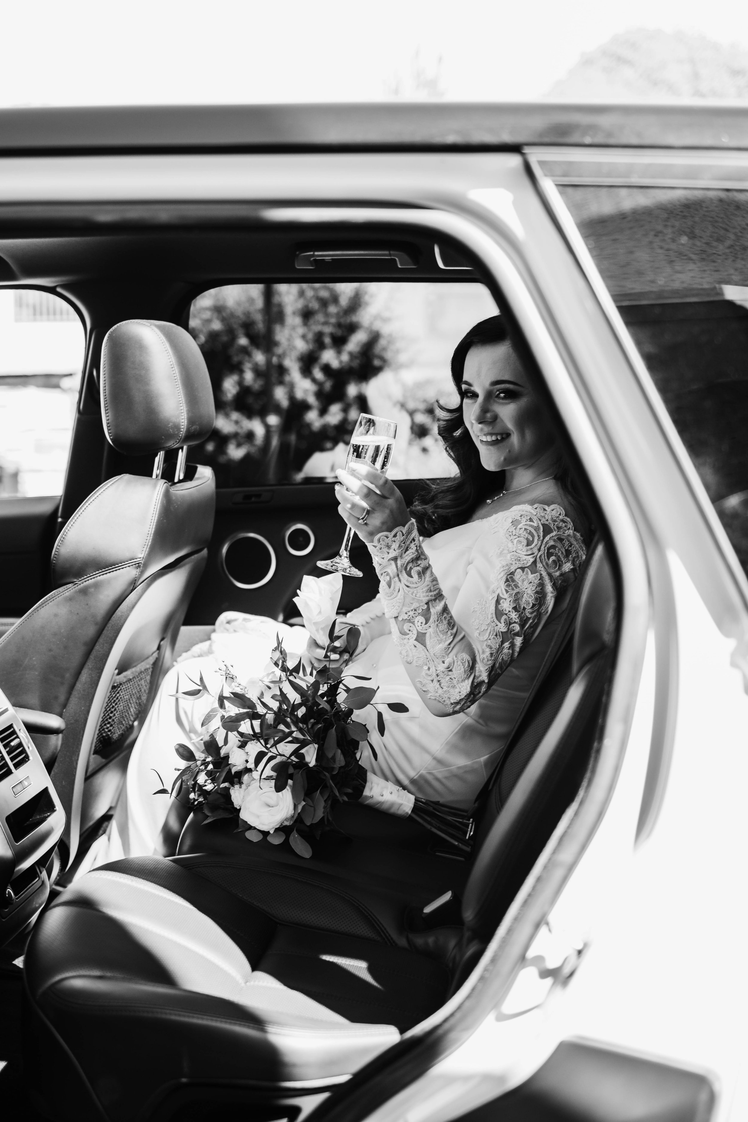 Bride sitting in the back of a fancy vehicle cheers-ing with a champagne glass