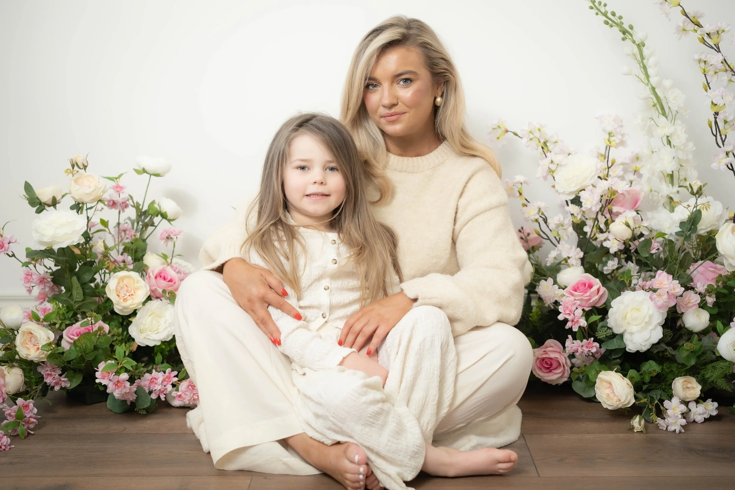 A woman and a young girl sitting on the floor surrounded by pink and white flowers.
