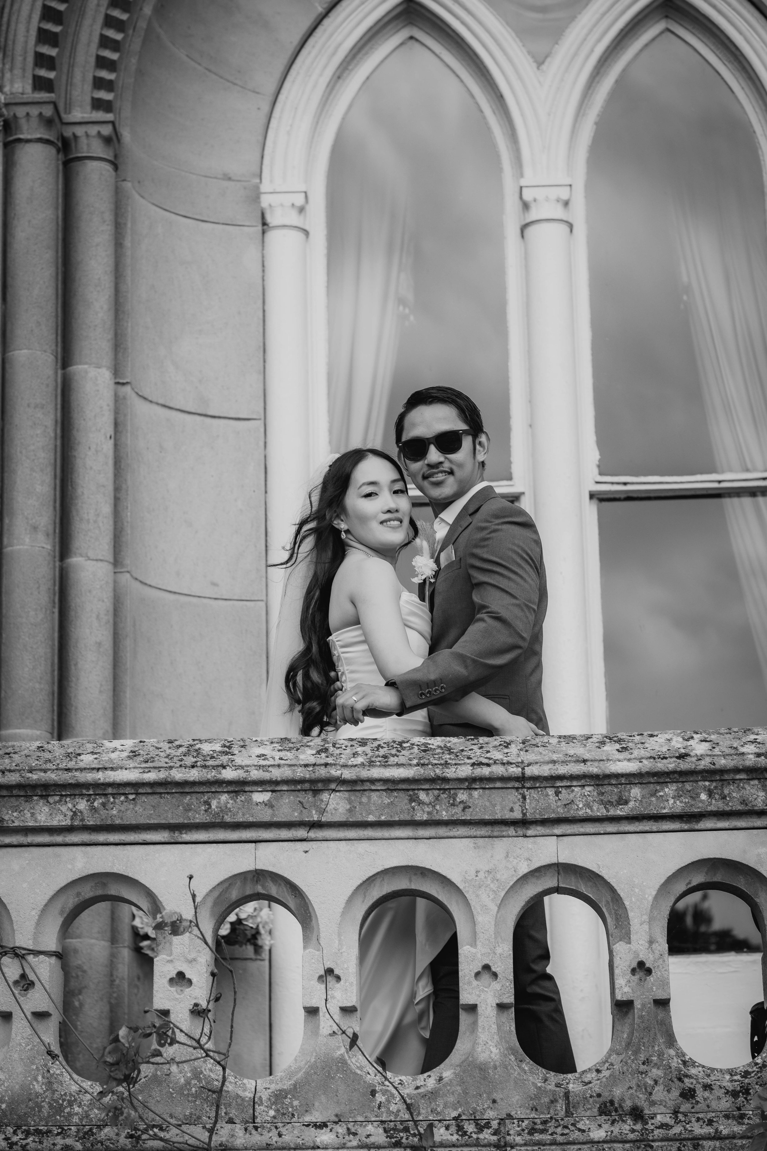 A bride and groom share a moment on a stone balcony as their wedding photographer captures the memory.