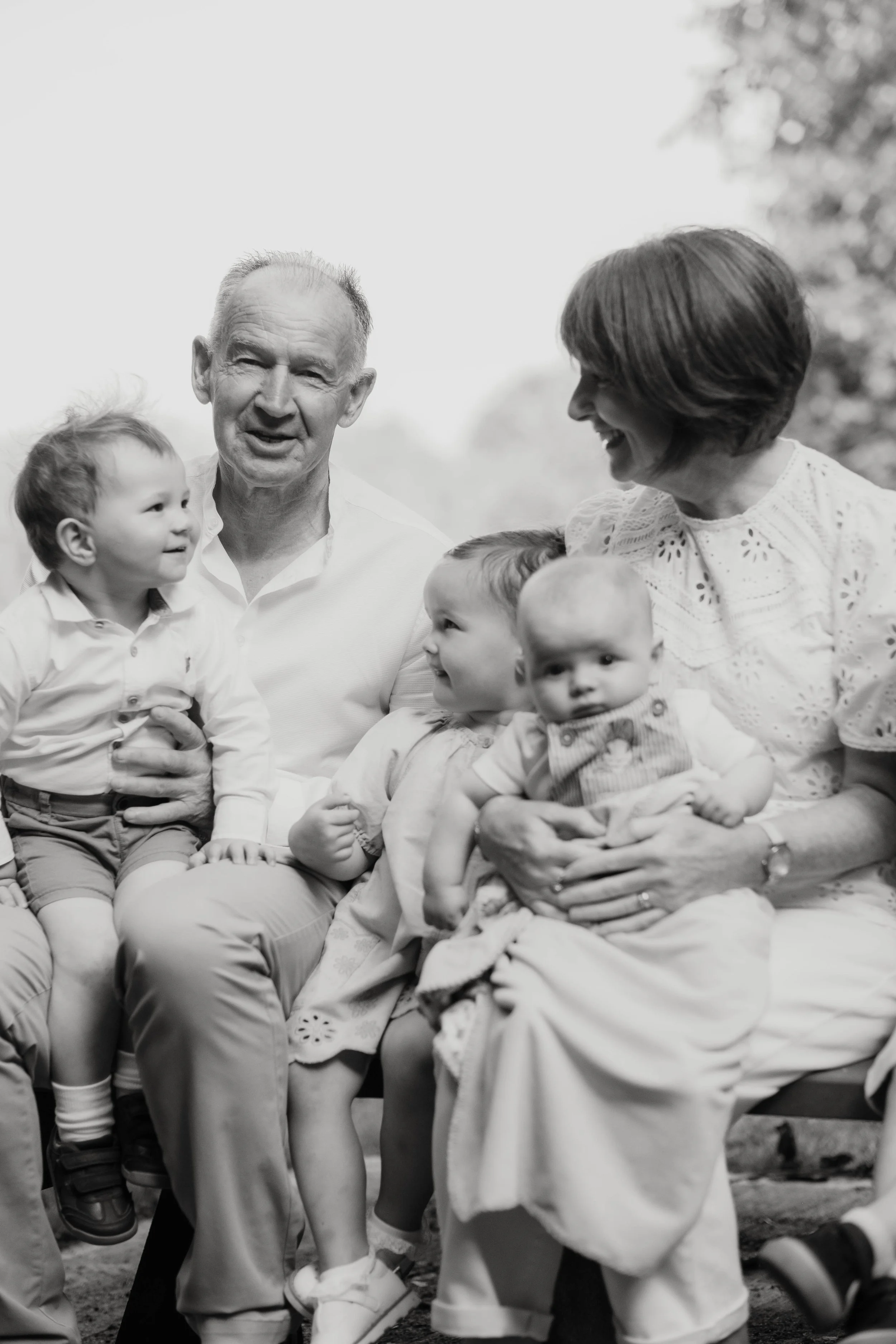 A black and white photo of three children and two adults sitting outdoors, smiling and engaging with each other.
