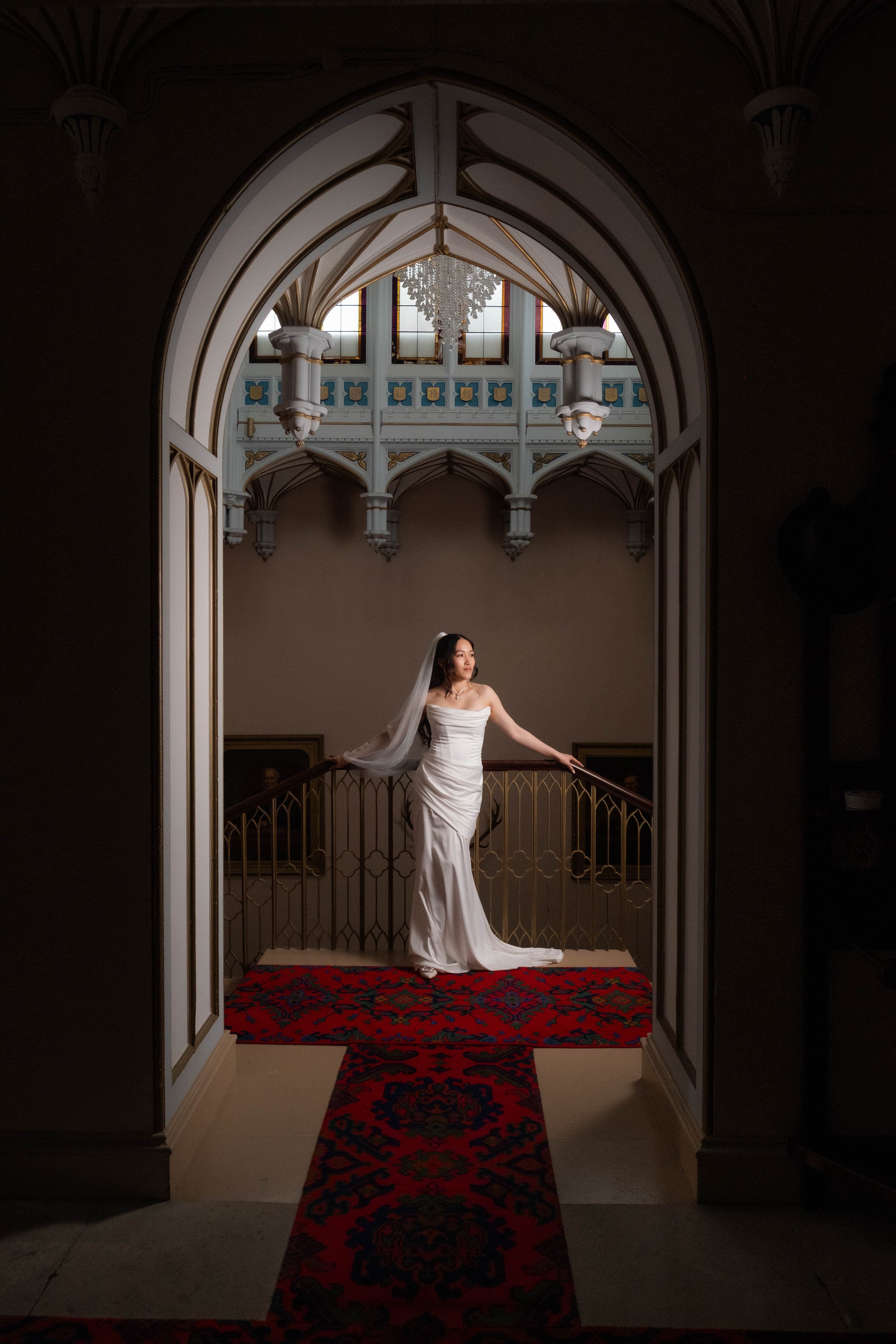 A bride in white stands gracefully under an arched doorway, softly lit—captured perfectly by a skilled wedding photographer.