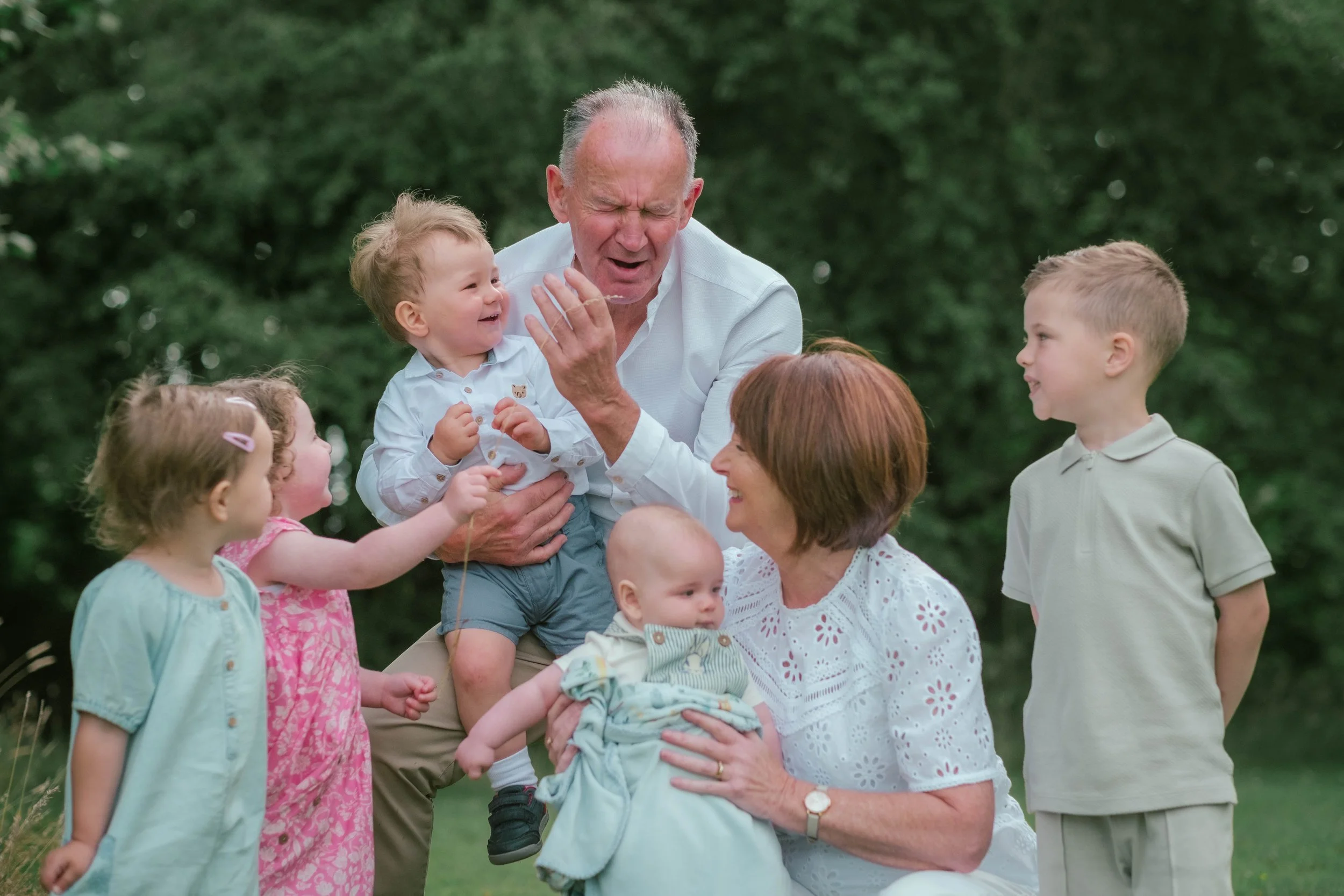 Family outdoor gathering with senior couple and young children, laughing and playing together in a park.