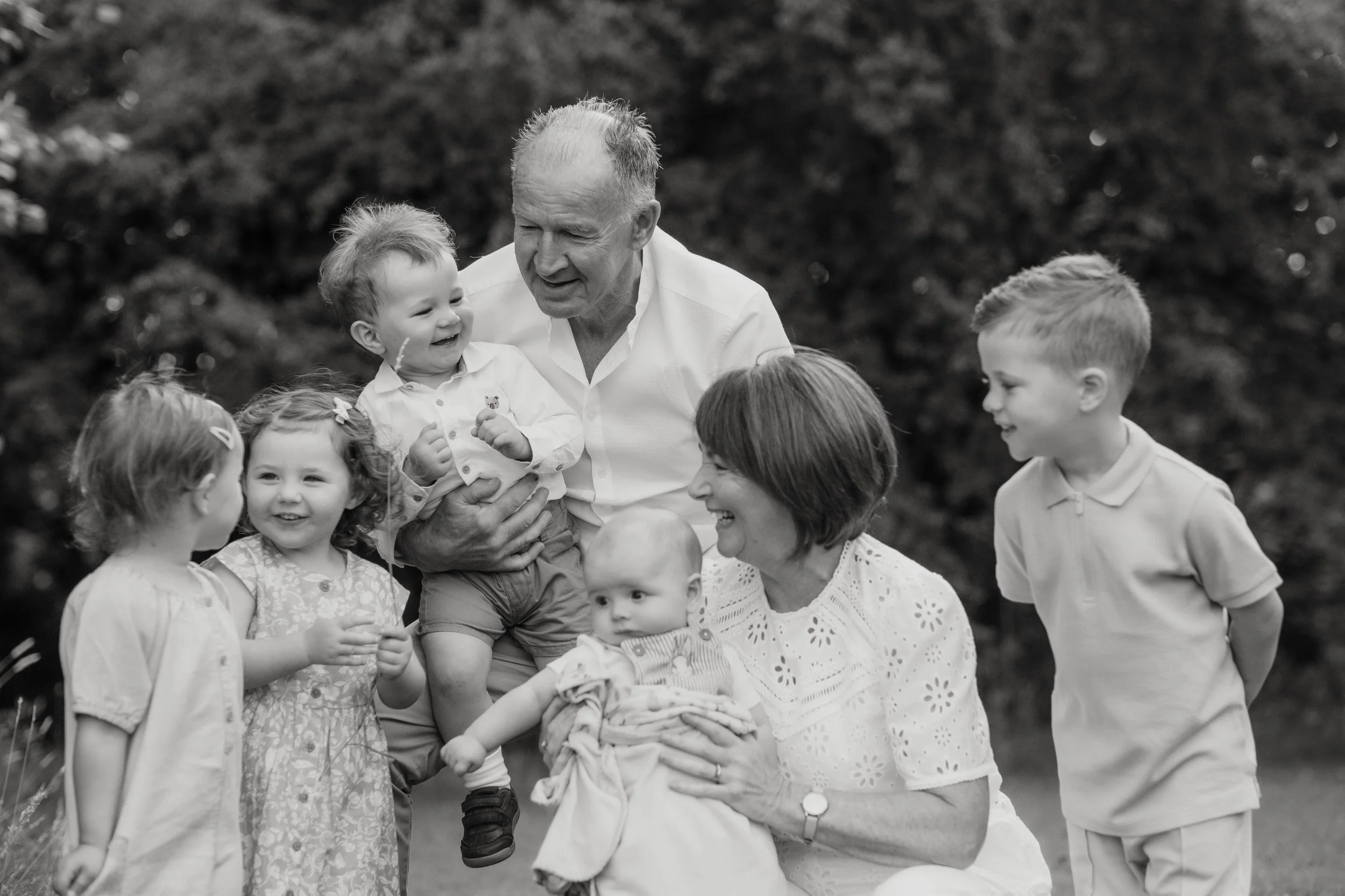 A black-and-white photo of three adults and five children outdoors, smiling and interacting closely.