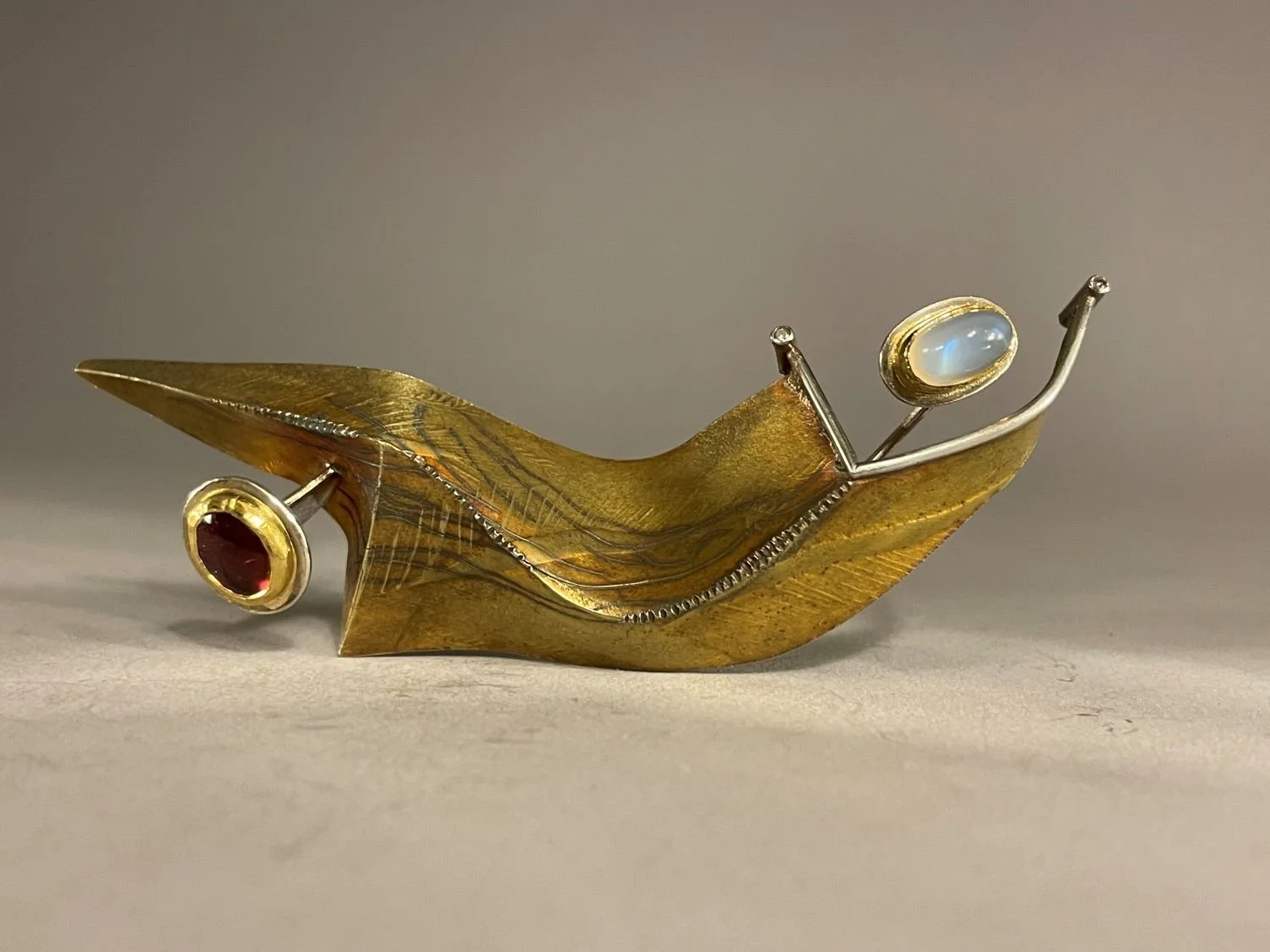 ‘Thrust’ Brooch (Swoop Series), 1994, materials 18k gold laminate, sterling, 24k Bezels, Moonstone and Rhodolite Garnet
Oval, 3.75 x 1.25 x 1 inches (9.5x3x2.5cm), $2800 Cdn.