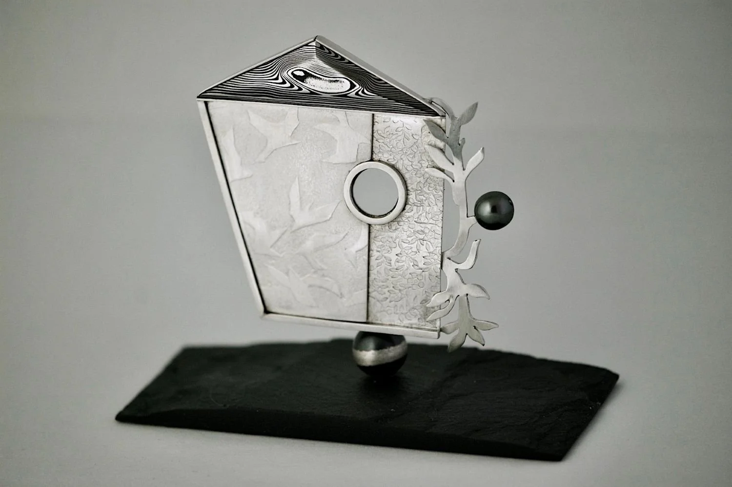 Bird House Brooch With Stand (JDA99), 2025, sterling, Damascus steel, pearl, slate, 2.75 x 2.5 x .75 inches (6.8X6.2X.8 cm) brooch, inspired by the work "Flight Of Seasons" by D. Helen Mackie RCA, $1500 Cdn.