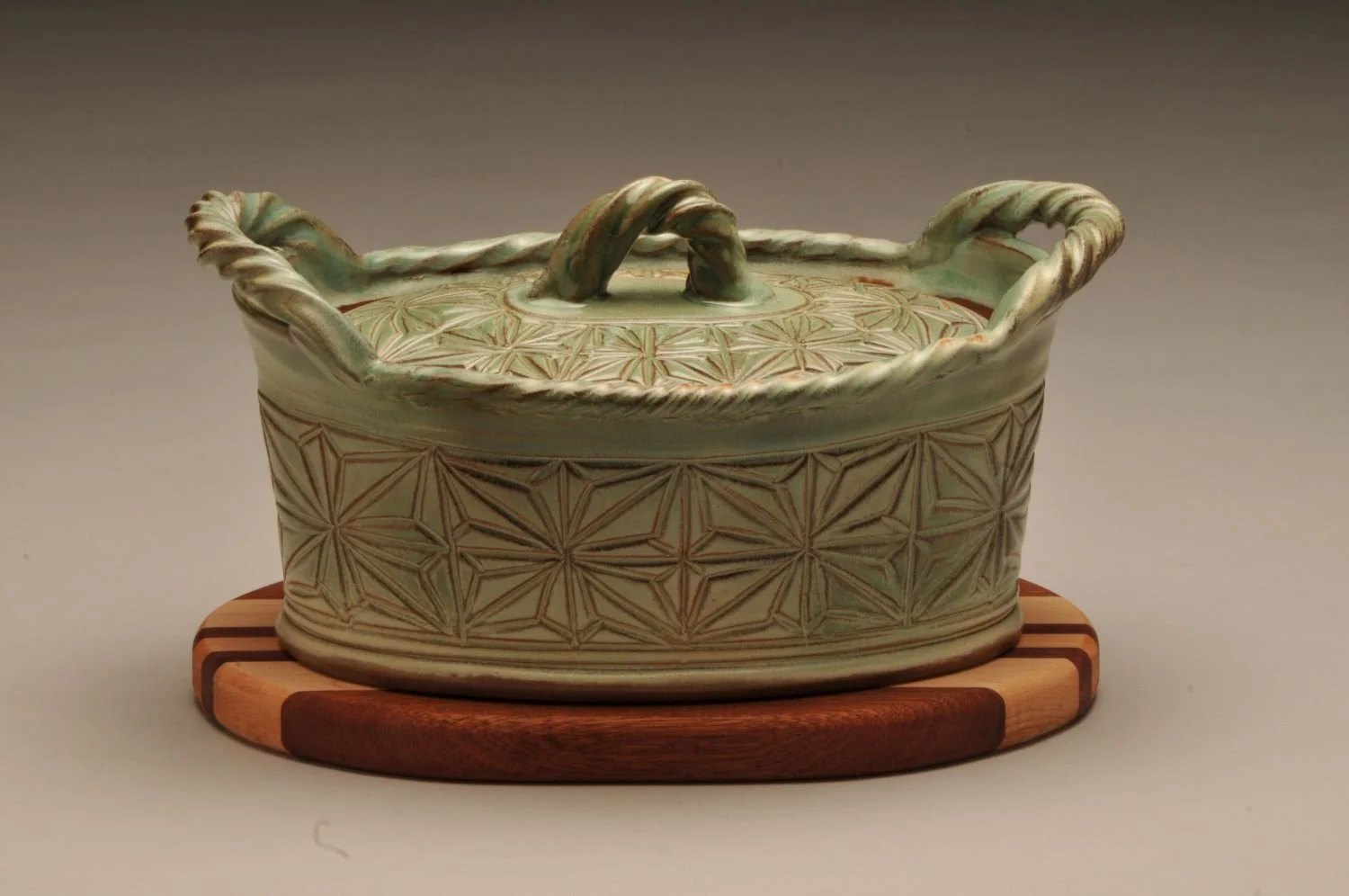 Kumiko Green Fields Casserole Dish With Striped Wood Trivet (#24.06.22), hand carved stoneware with handmade oak, cherry, walnut trivet, 5.5 x 9 x 5.5 inches (14 x 23 x 14 cm), sold.