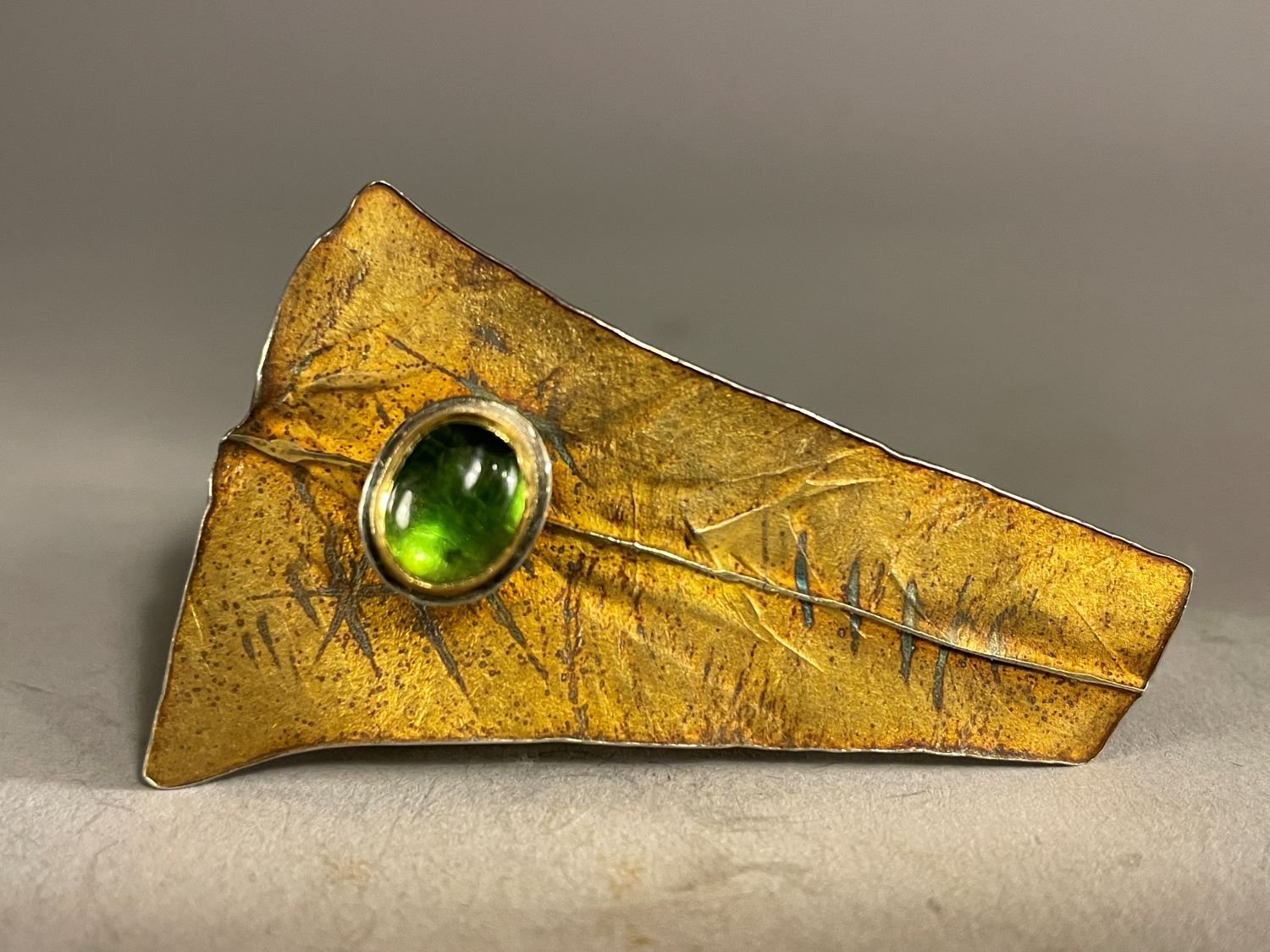 ‘Hide’ Brooch (Swoop Series), 1994, materials 18k gold laminate, sterling, 24k bezels, green oval tourmaline, 2.25 x 1.25 x .75 inches (5 x 3.5x2 cm), $1300 Cdn.
