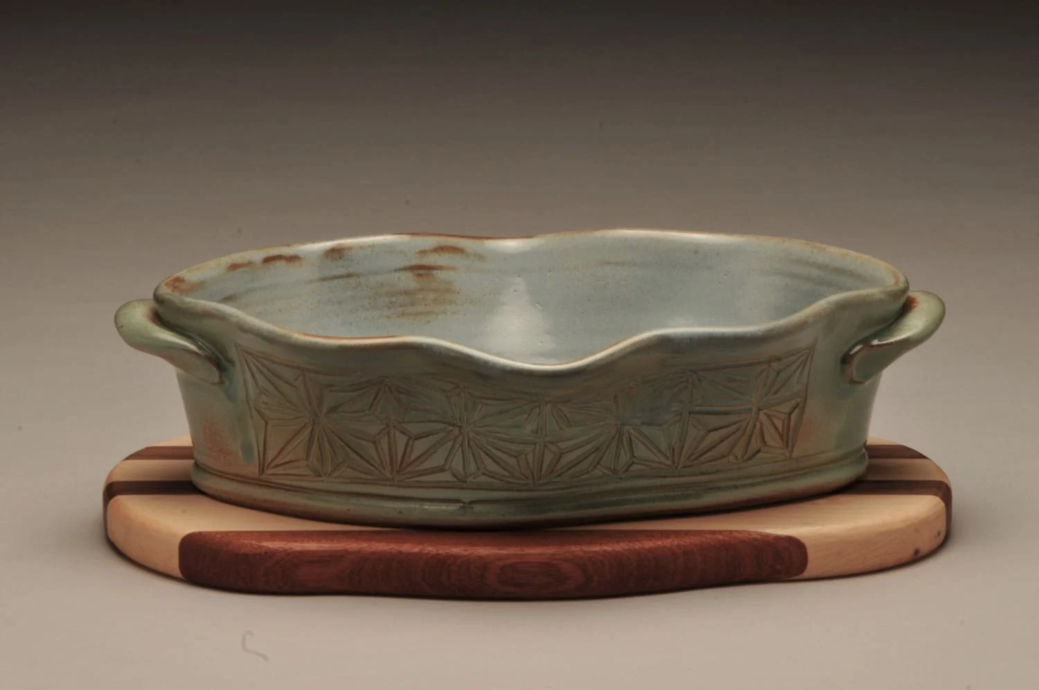 Kumiko Wavy Bowl With Striped Wood Trivet (#24.07.02), hand carved stoneware with handmade walnut, cherry, and oak trivet, overall 4 x 11 x 7 inches (10 x 28 x 18 cm), $200 Cdn.