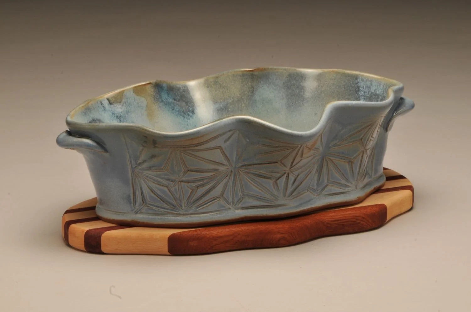 Kumiko Blue Skies Wavy Bowl With Striped Wooden Trivet (#24.06.20), hand carved stoneware with handmade oak, cherry, walnut trivet, 4.5 x 11 x 8 inches (11.5 x 28 x 20 cm), sold.
