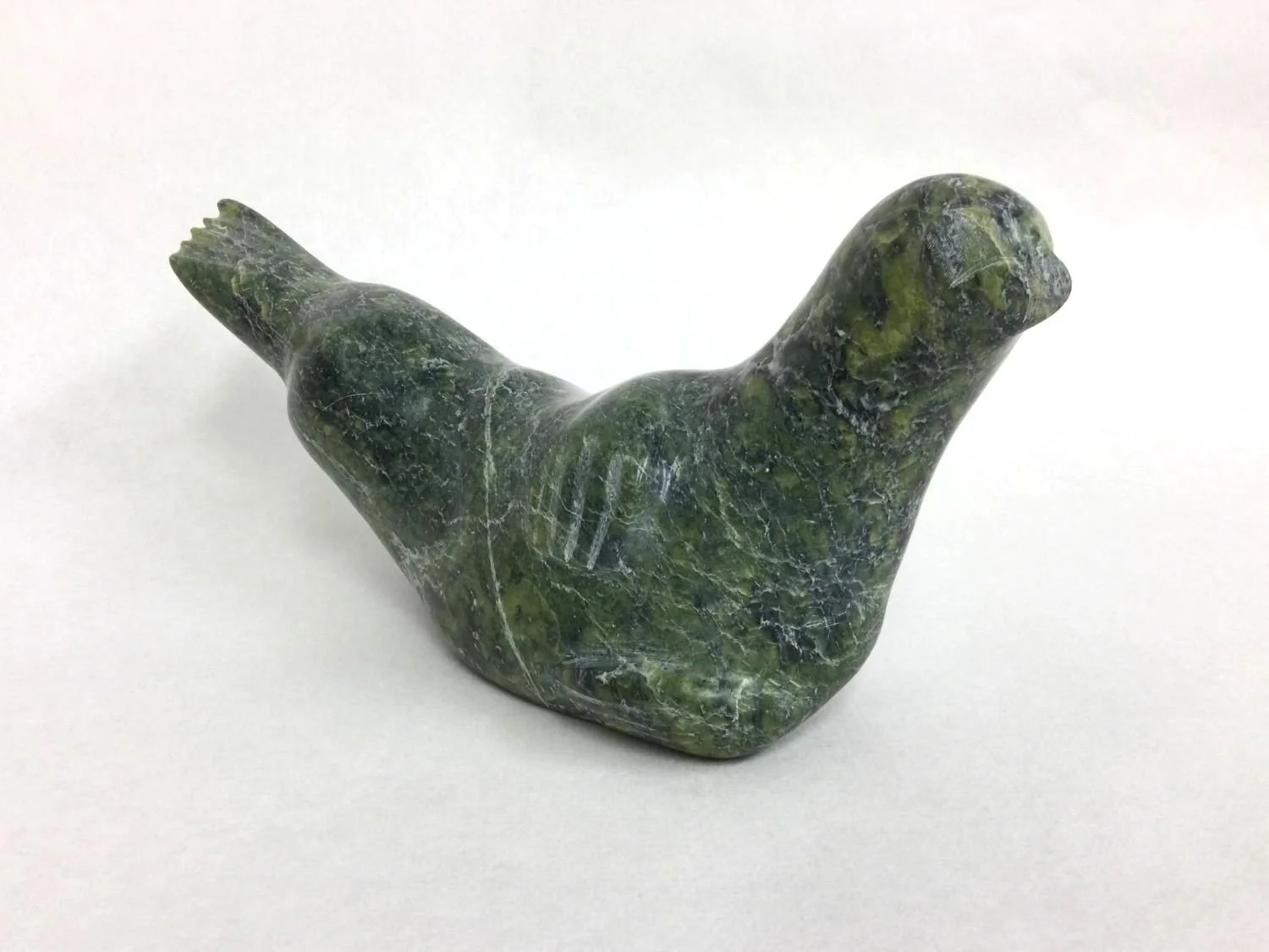 Lucassie Ikkidluak (E7-765) ᓗᑲᓯ ᐃᑭᓗᐊ (1949-) Kimmirut / Lake Harbour ᑭᒻᒥᕈᑦ, Seal (#25.6.11), c.1965, green serpentine, 5 x 3.25 x 10 inches (12.5 x 8 x 25.5 cm), provenance: Saskatchewan Collection, $950 Cdn.