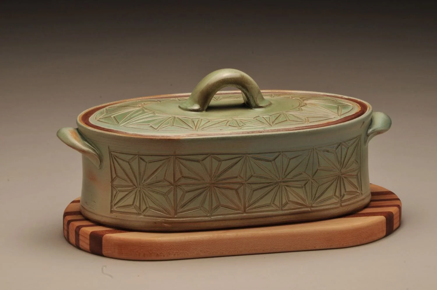 Kumiko Green Fields Casserole with Striped Wood Trivet (#24.07.01), hand carved stoneware with handmade oak, cherry, and walnut trivet, overall 5 x 12 x 7 inches (13 x 30.5 x 18 cm), $275 Cdn.