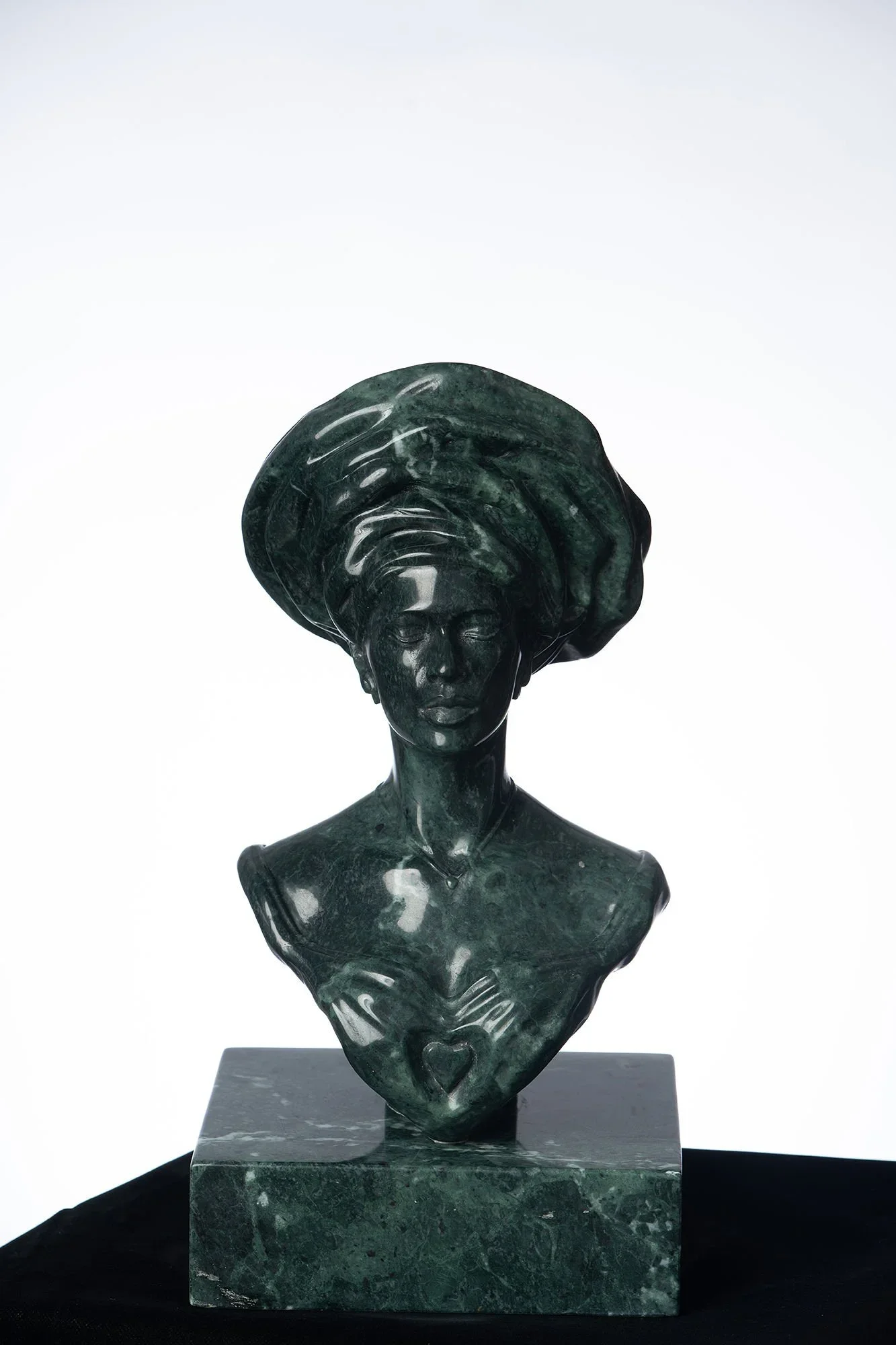 Green marble bust sculpture of a woman with an elaborate hairdo and a heart symbol on her chest, on a matching green marble base.