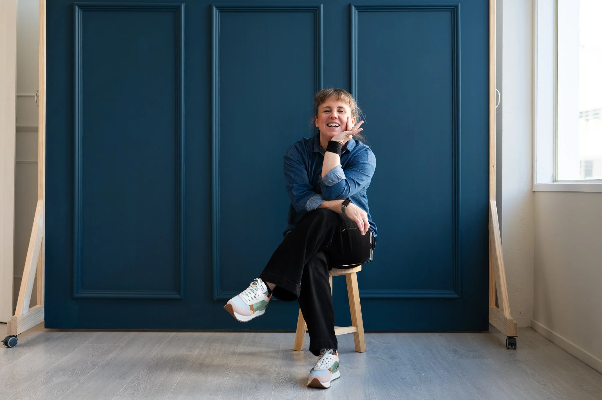 Nykie sitting on stool with legs crossed looking happy.