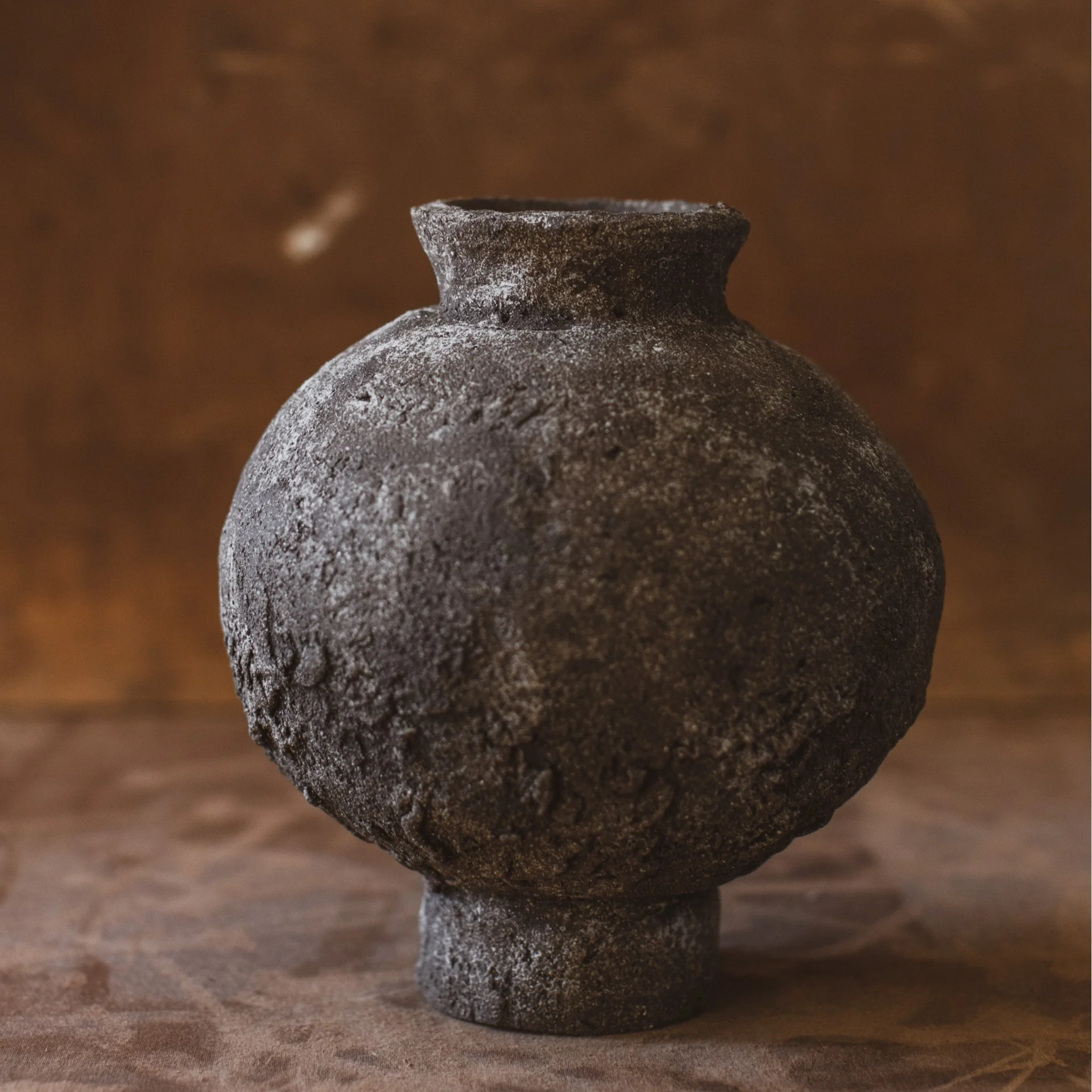 Dark spherical moon jar, natural finish with speckled white porcelain. Ceramic vase has rough exterior.