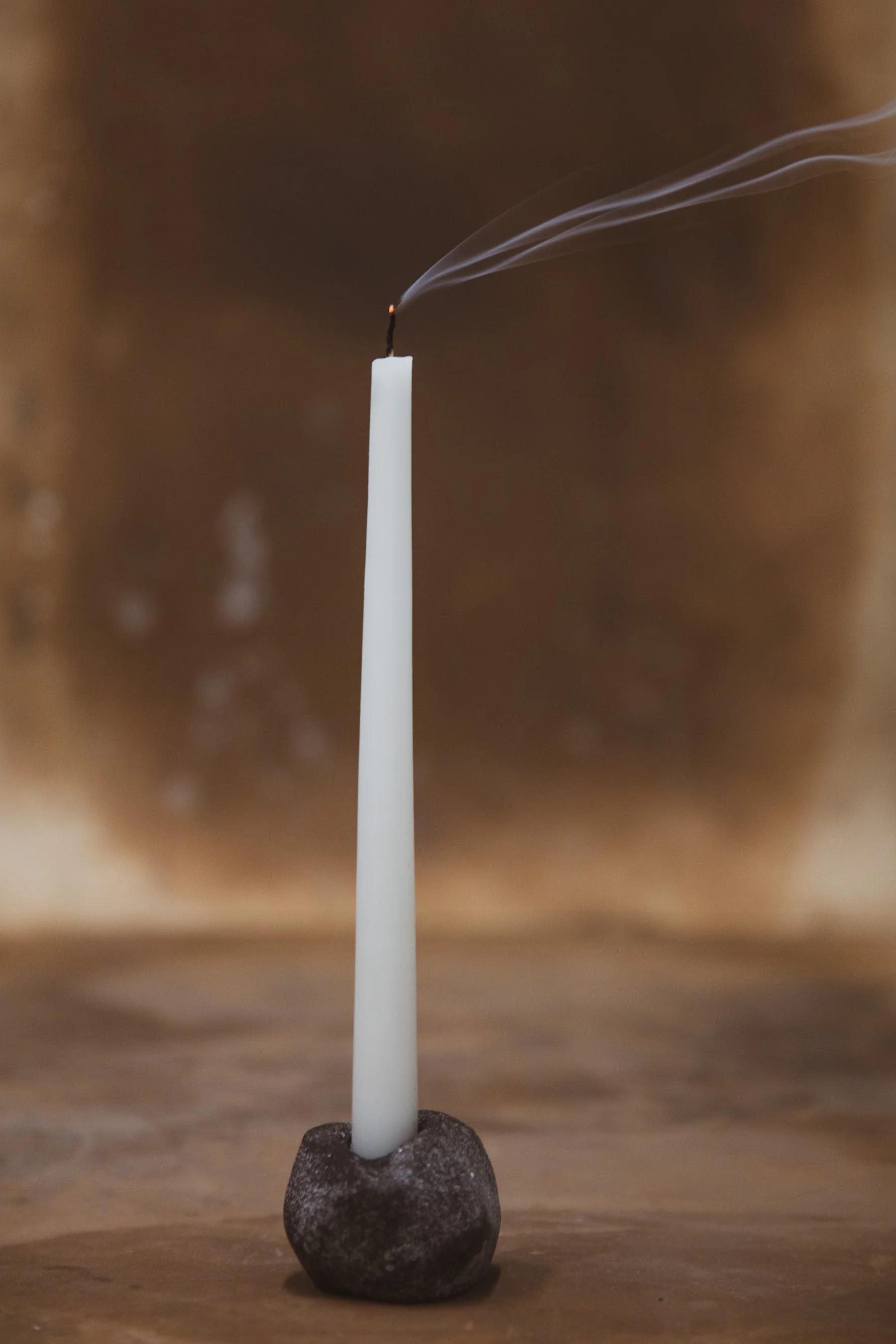 A small dark ceramic candlestick holder with a candle