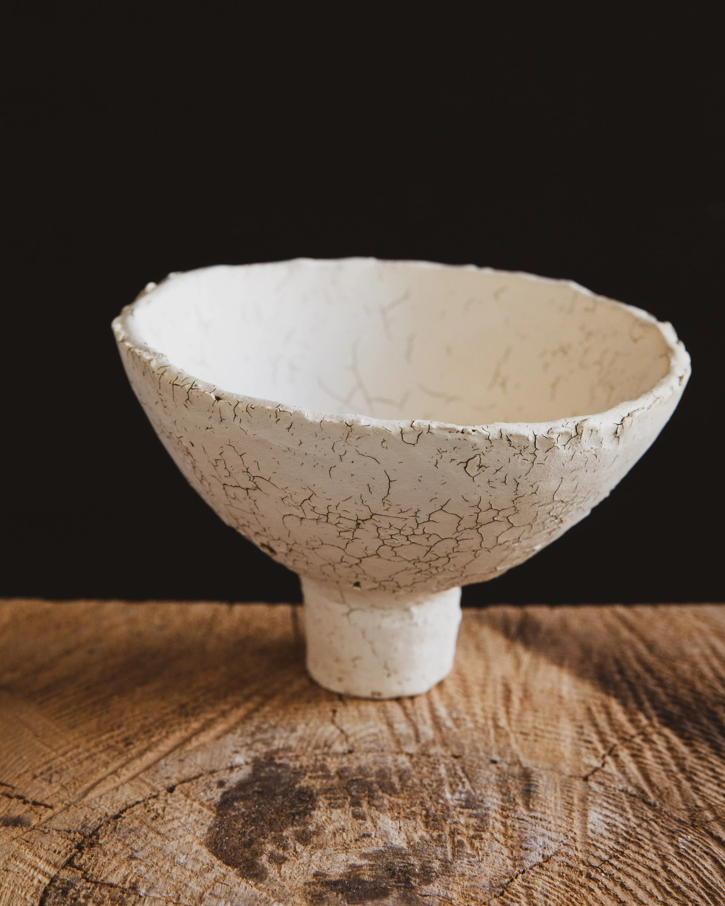 A white ceramic vessel with a dark cracking pattern