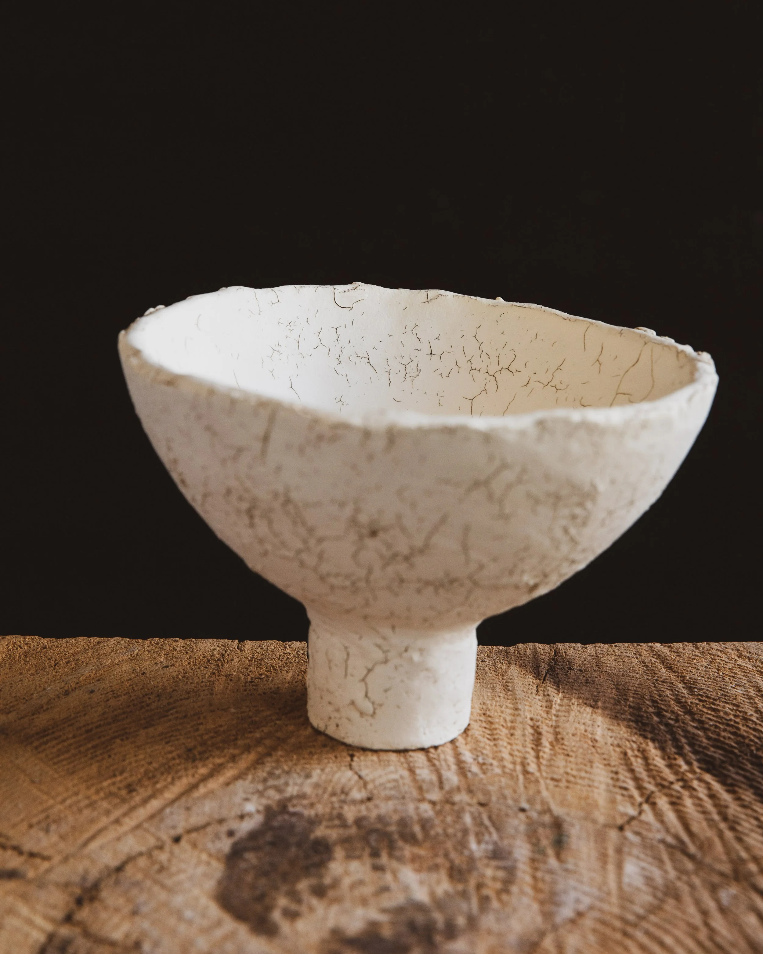 A white ceramic vessel with a dark cracking pattern