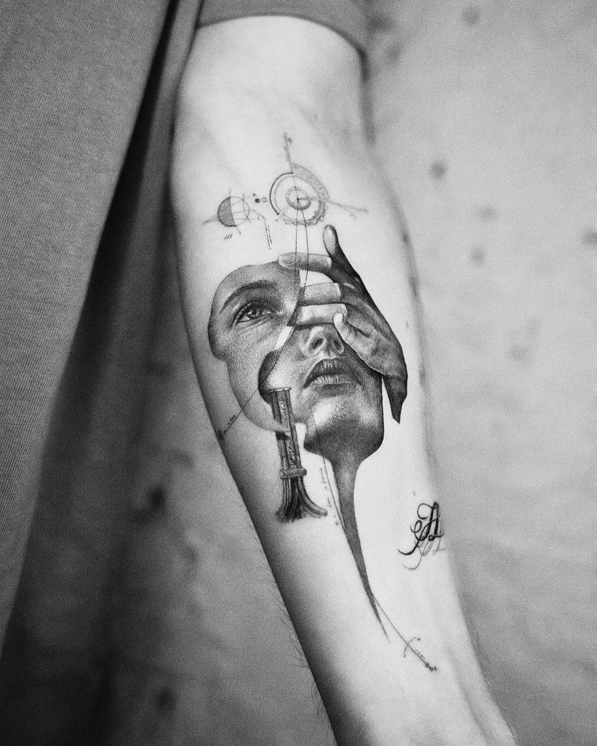 A black and white tattoo of a woman's face with a robotic and abstract design, including gears, lines, and geometric shapes, on a person's forearm.