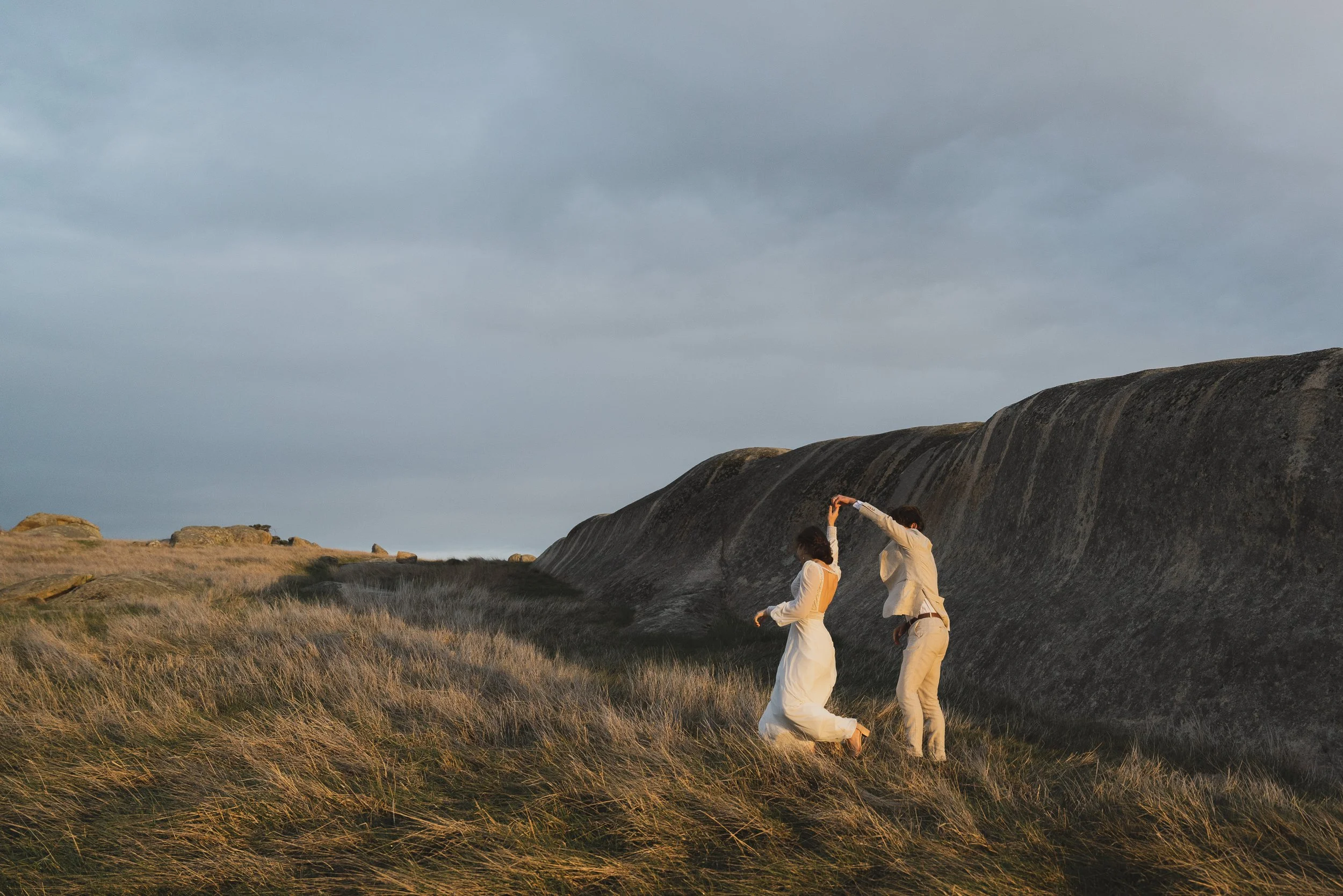 Jed and Alysha dancing in the dusk light by a large, grey boulder.