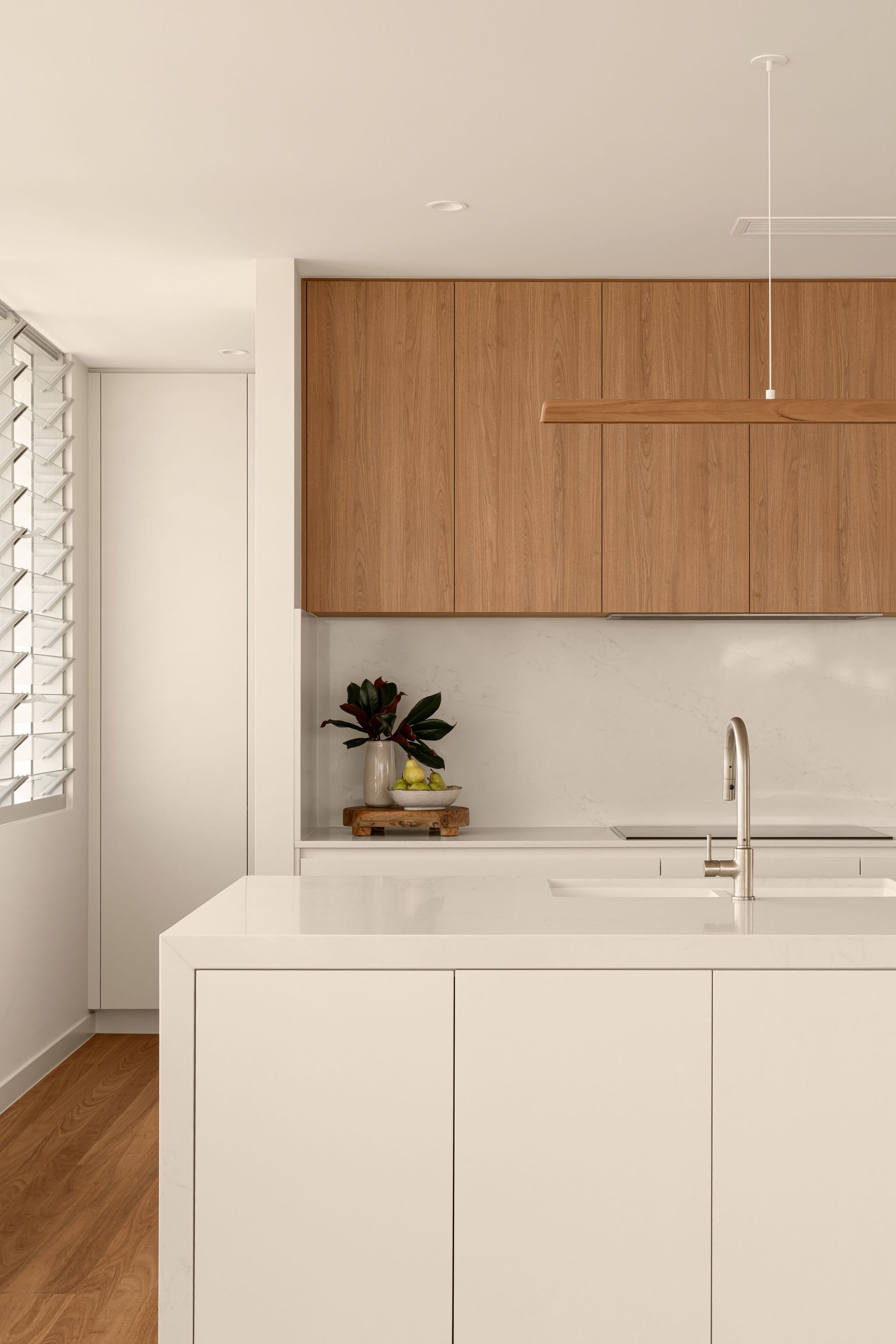 Front-facing view of the sleek island bench with integrated sink, showcasing warm timber cabinetry and a sculptural timber pendant light above