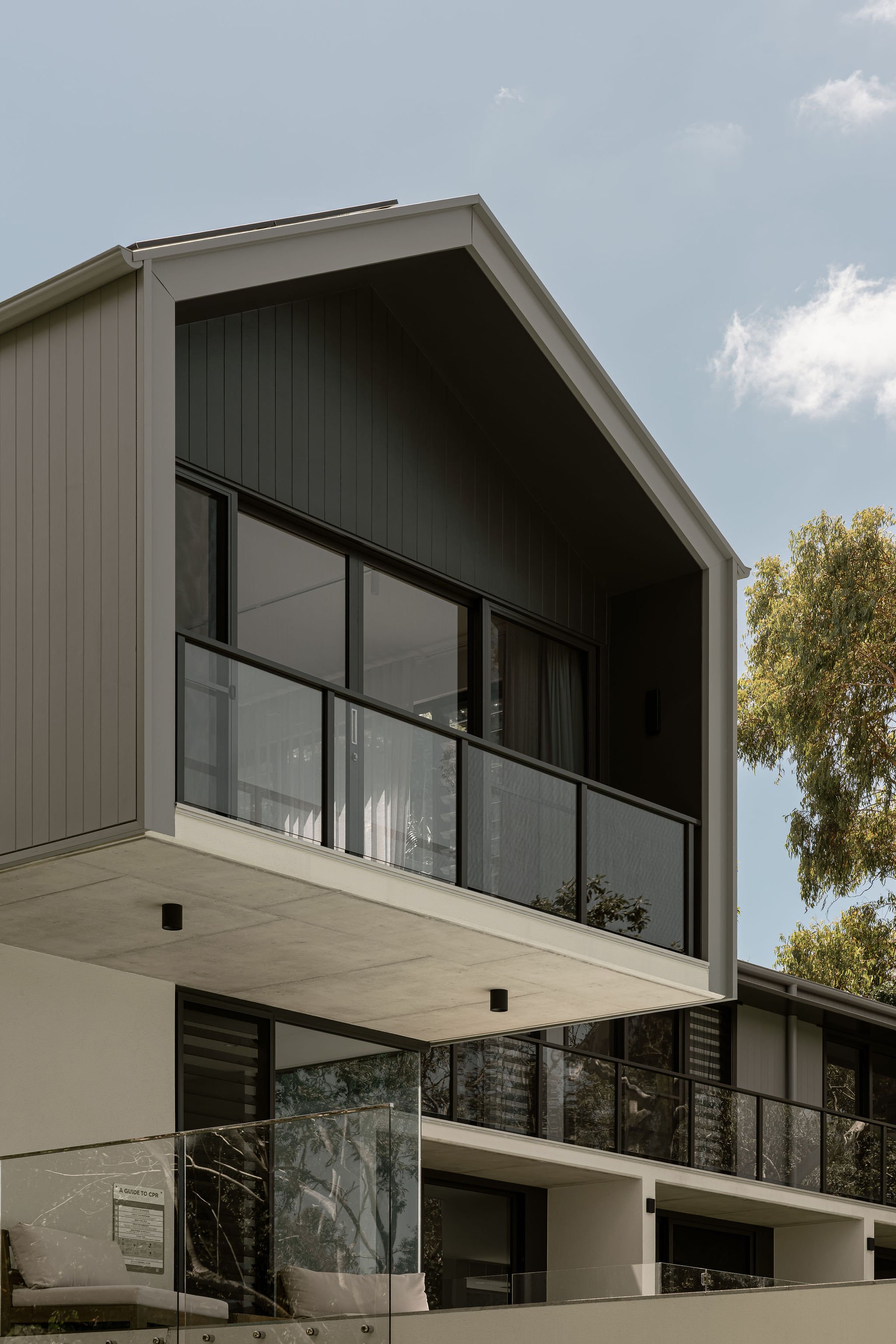 Close-up view of the architectural gable roofline with matte grey vertical cladding and glass balustrades on the upper balcony