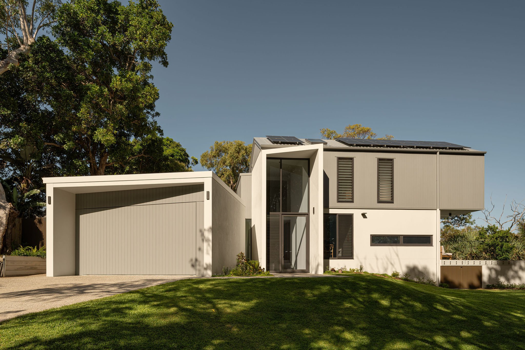 Contemporary home exterior with clean lines, solar panels on a gabled roof, and lush green lawn in the foreground