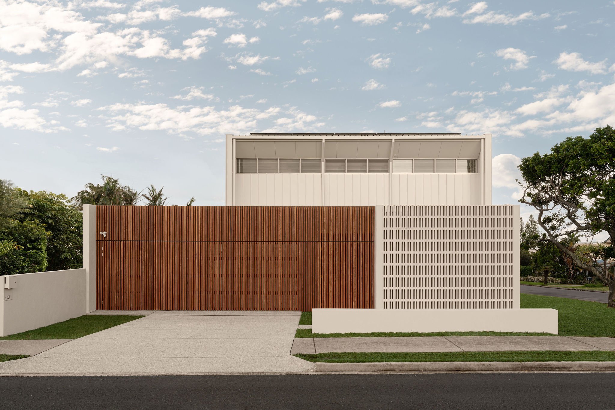 Full view of the residence from the street, featuring a timber batten garage door and textured concrete screen alongside a white metal-clad upper level