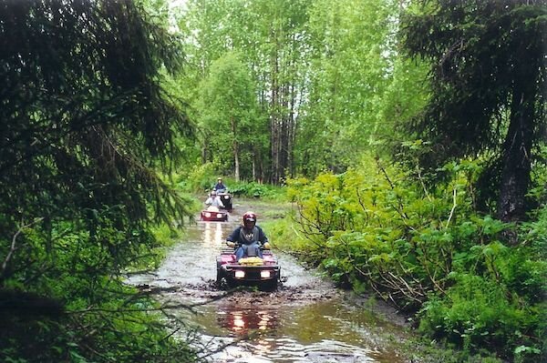  ATV riders going through a large stream on a tour with Alaska Adventure 