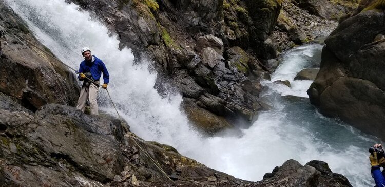  A person rappeling down a cliff next to a waterfall with Alaska Backcountry Access 
