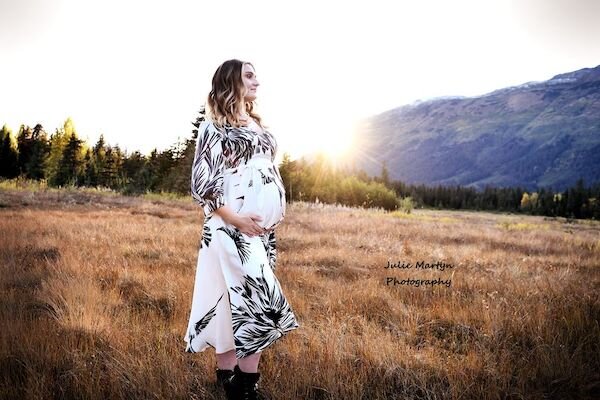  A pregnant woman in a field with the sun in the back ground with photo taken by Julie Martyn Photography 