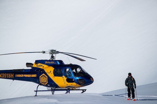  Skier next to helicopter on a mountain with Chugach Powder Guide 