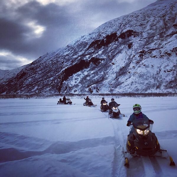  Snow Mobile riders following each other through a field of snow while Snowmobiling with Glacier City Snowmobile Tours 