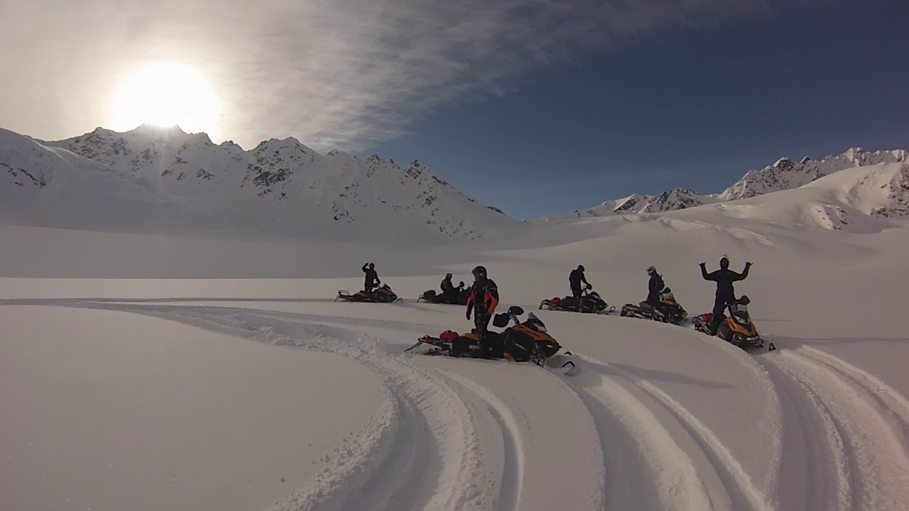  A group of people snow mobiling in a large, snowy field with Alaska Wild Guides 