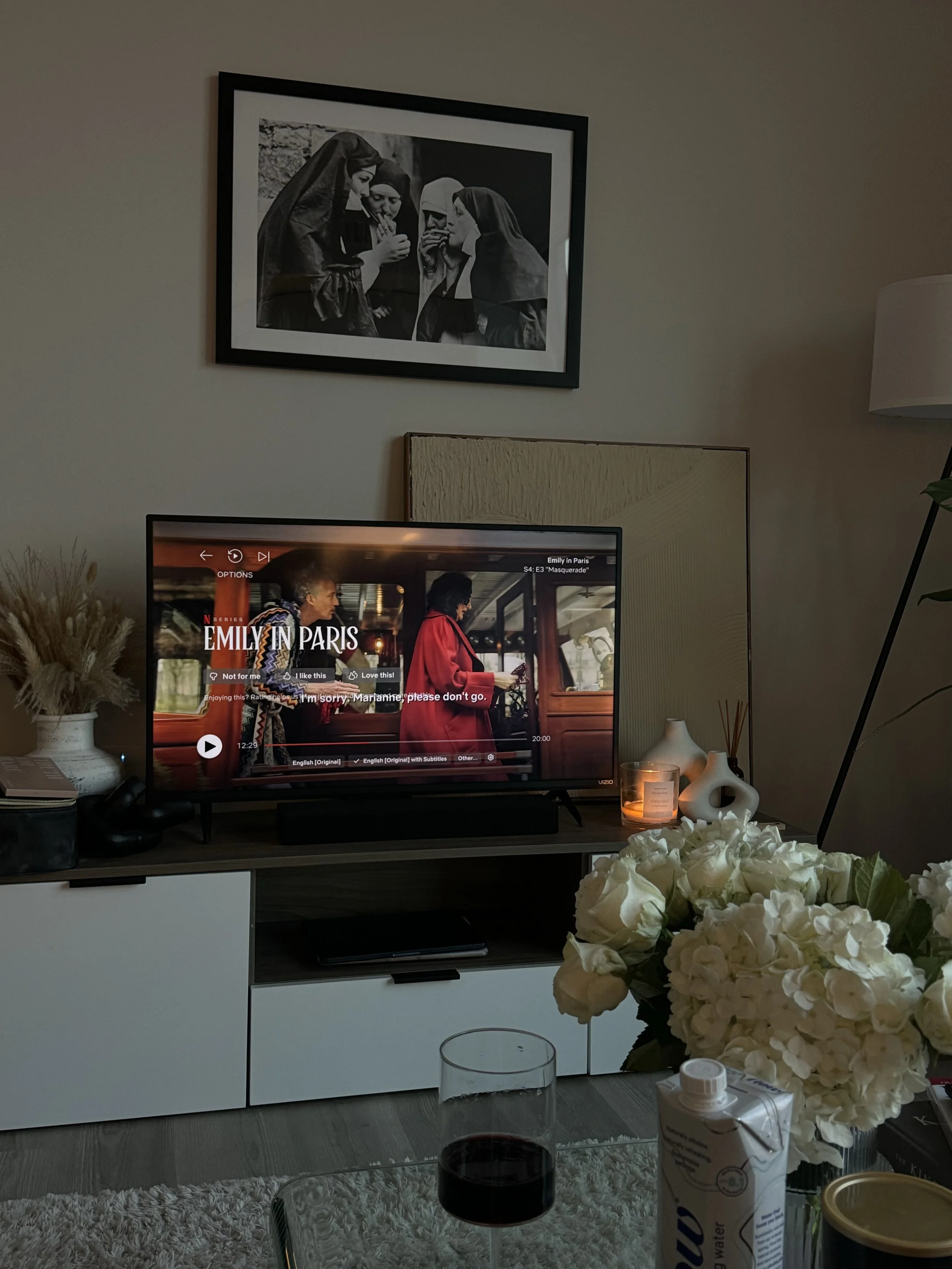 Cosy living room setup with flowers, candles, and TV showing Emily in Paris: slow evening routine aesthetic.
