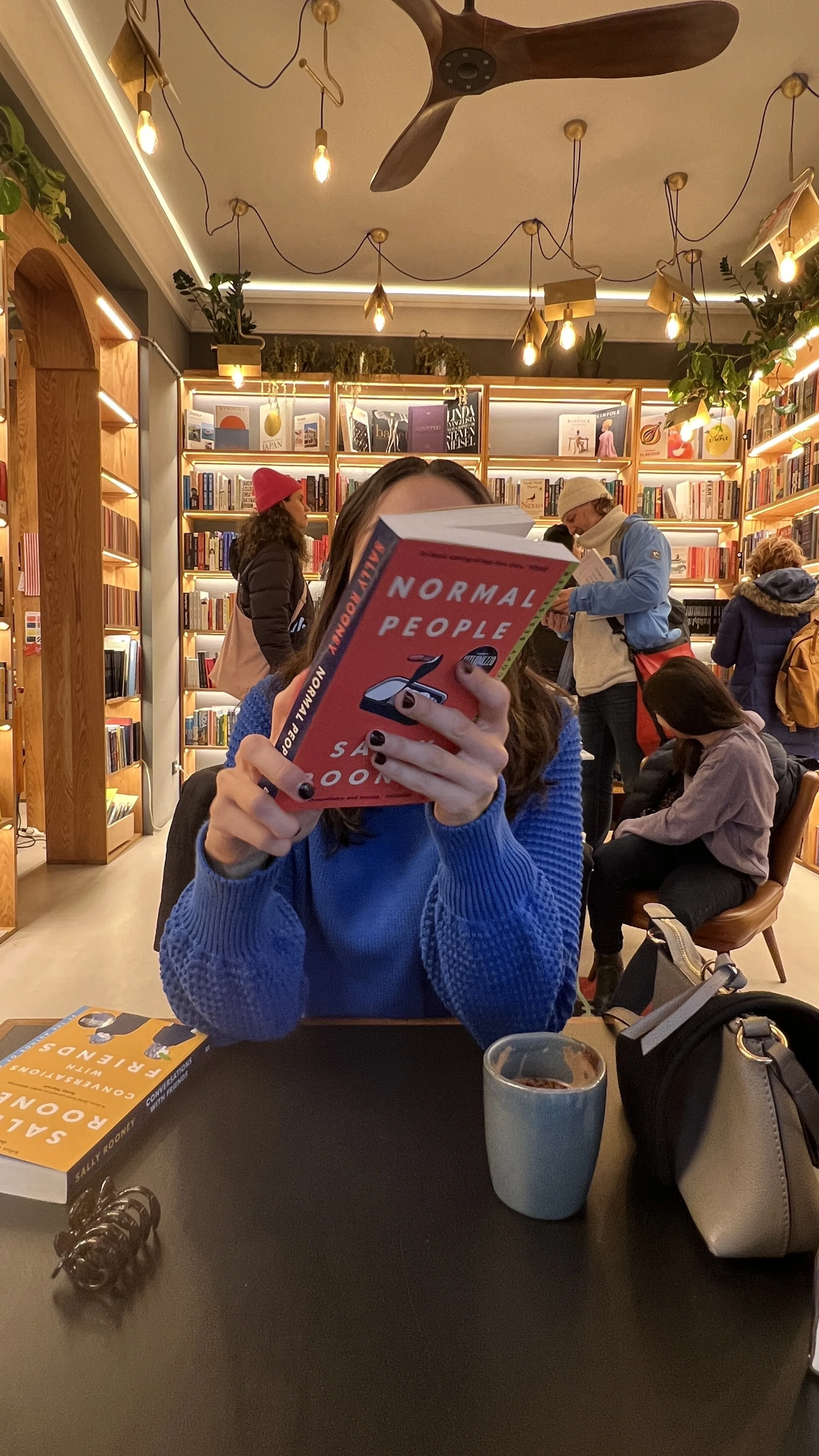 Woman reading a book in a cosy bookstore café: slow morning, soft life aesthetic, reconnecting with old hobbies.
