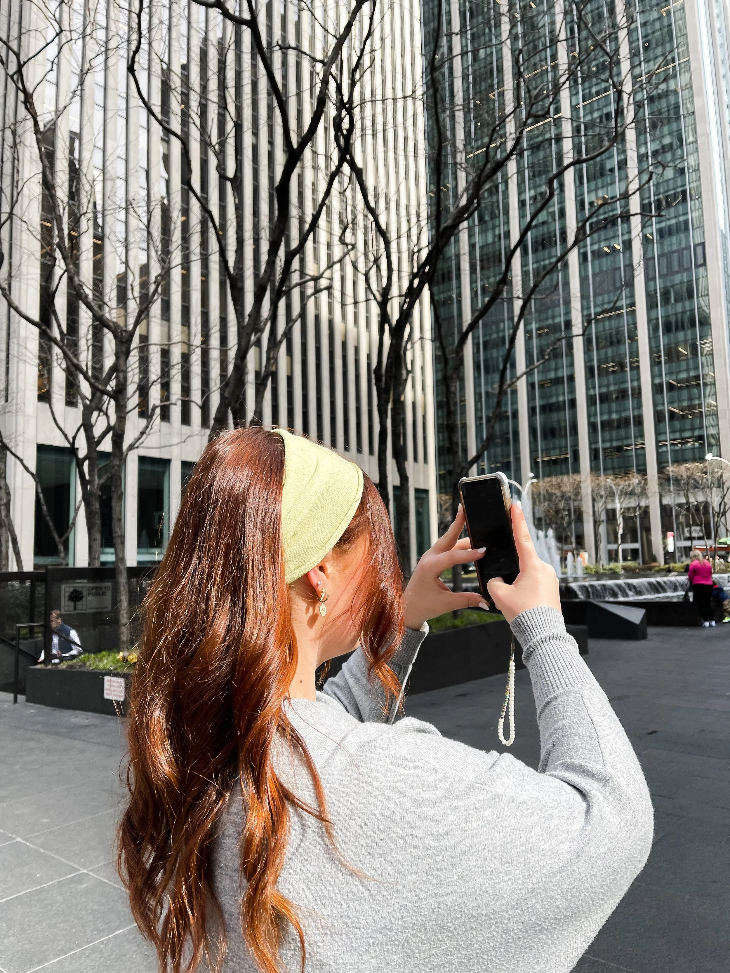 Woman photographing skyscrapers on a sunny day: capturing everyday beauty, mindful city living.
