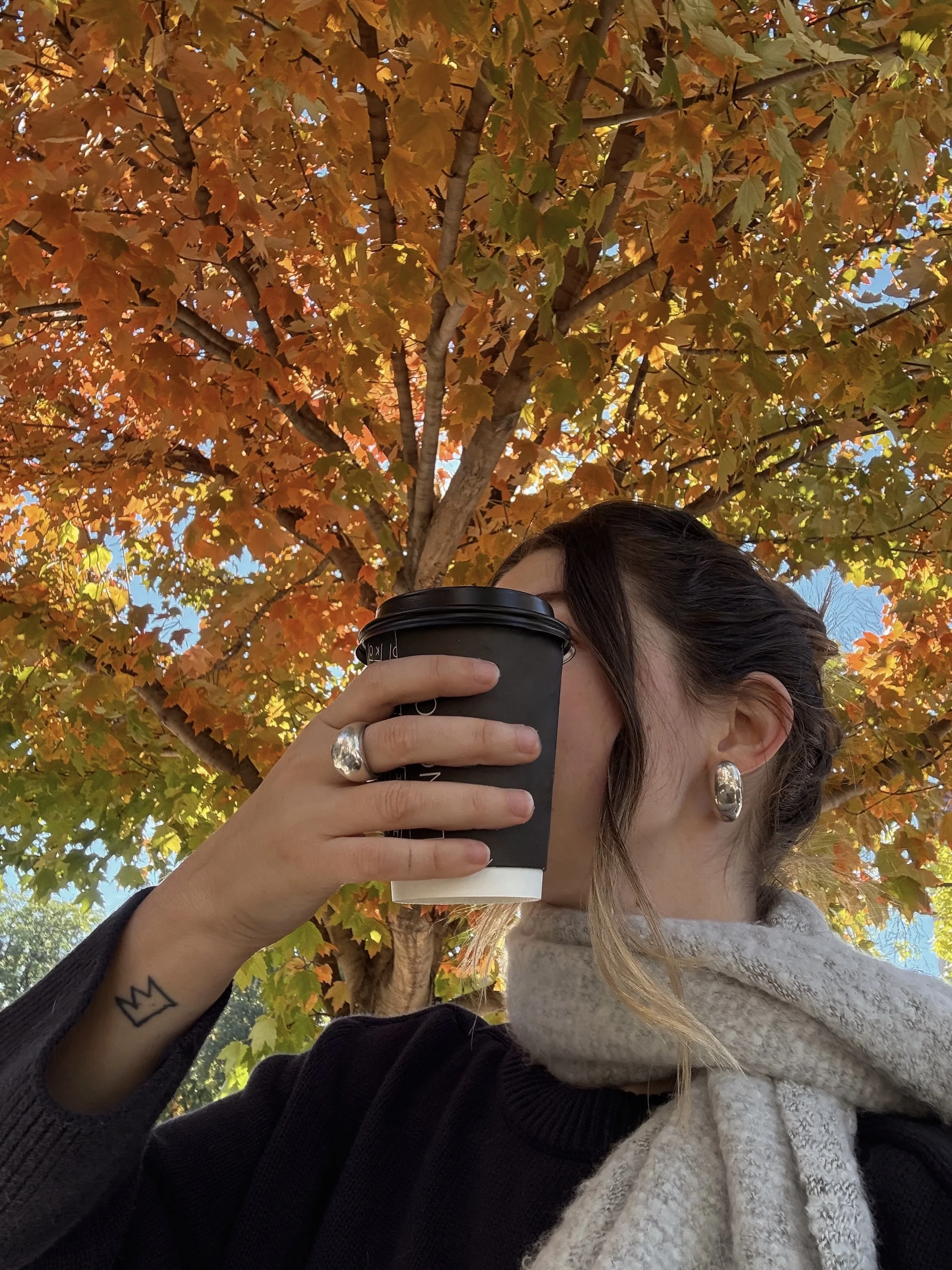Woman enjoying a warm coffee outdoors under autumn leaves: cosy fall vibes, self-care moment, romanticising everyday life.
