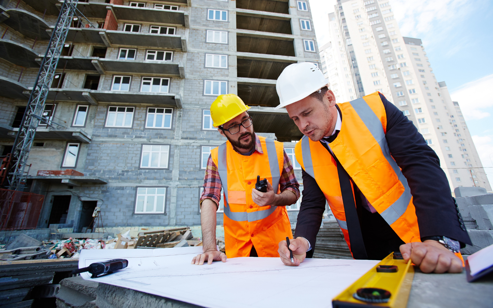 Two construction professionals in hard hats reviewing building plans at an apartment construction site.