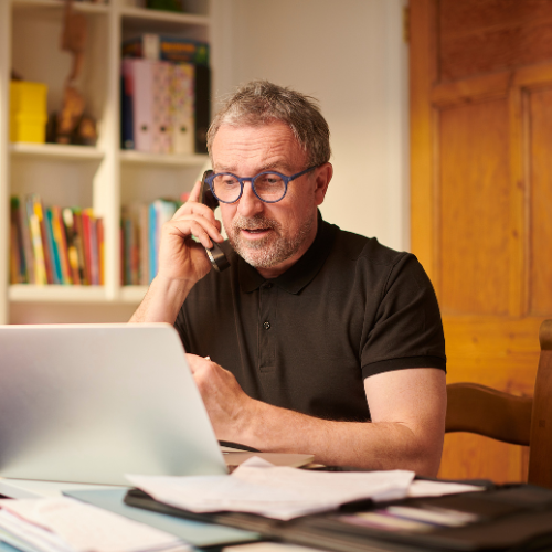 Property owner reviewing documents on a laptop while discussing a residential project by phone.