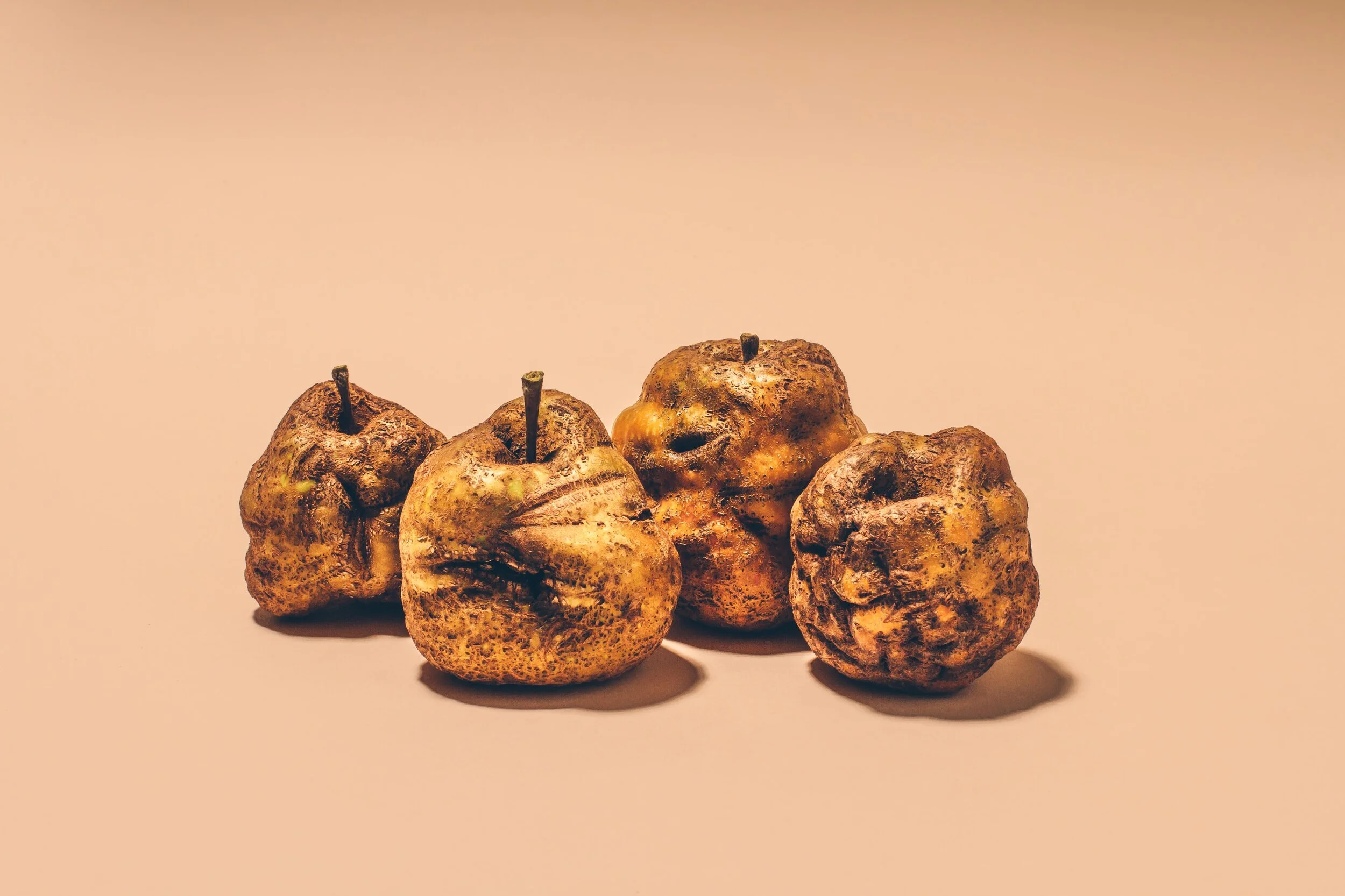 Four decayed, rotten apples against a neutral background.