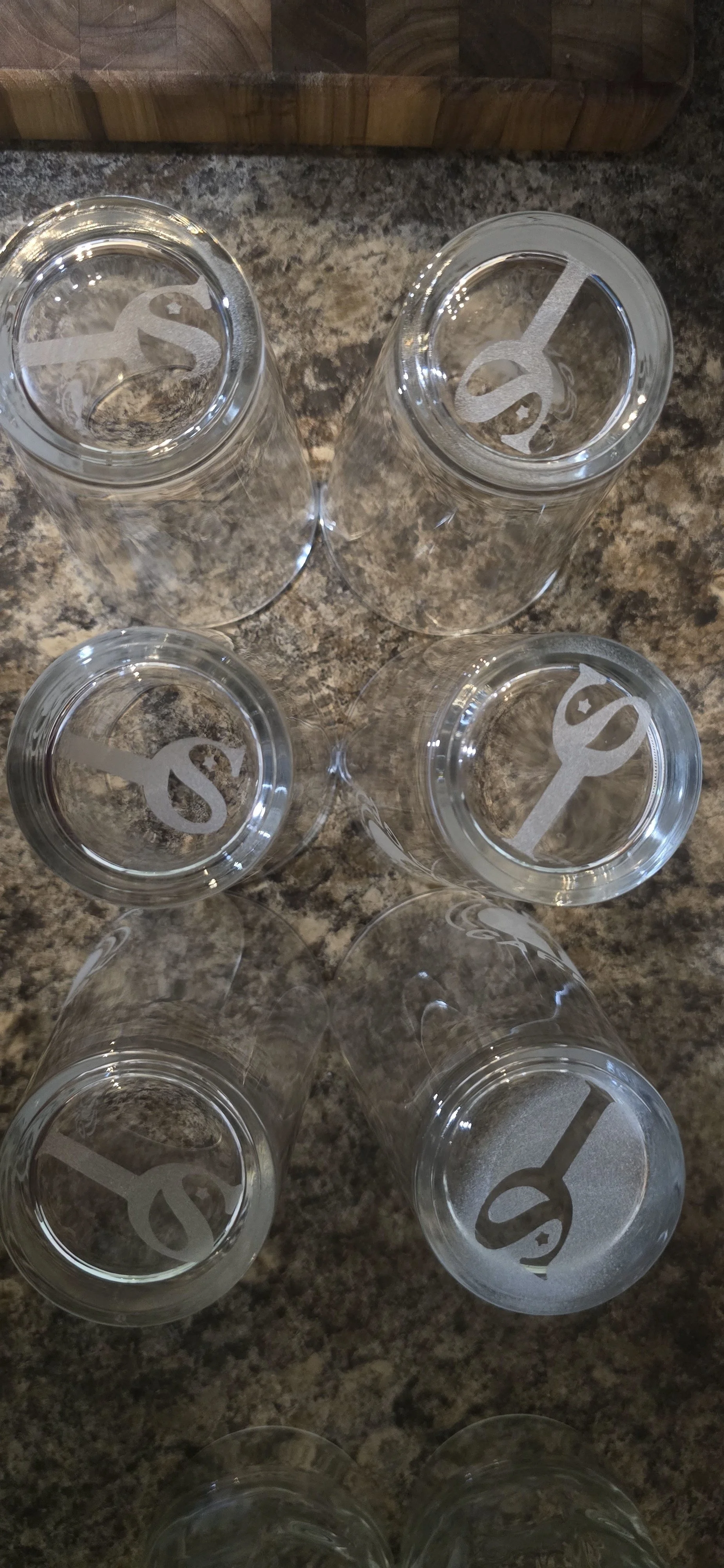 Six empty beer glasses with frosted isc logos on the bottom, arranged on a granite countertop in a hexagon shape.