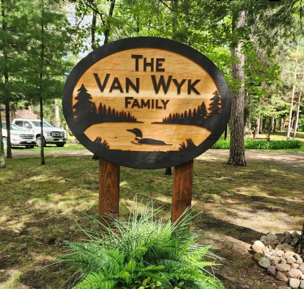 Personalized carved cedar sign with loon design mounted on wooden posts at a lake house or cabin entrance