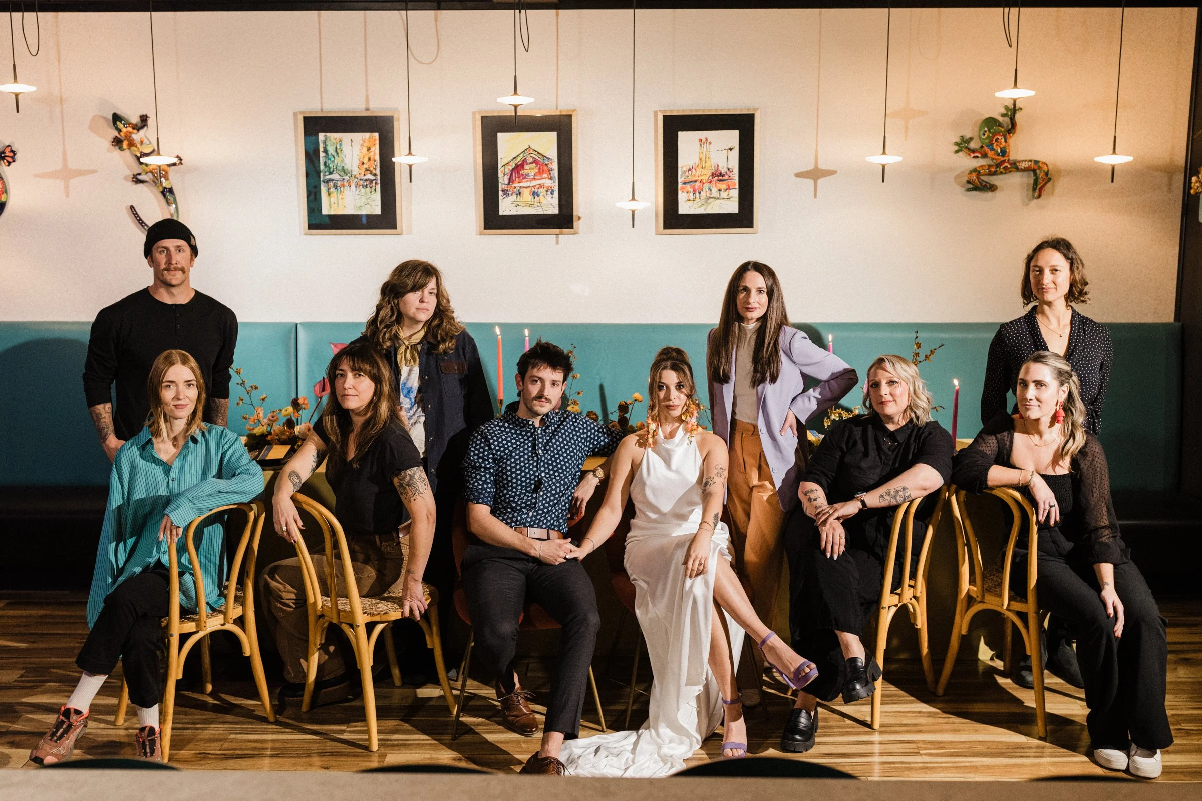 Group of ten people posing in a restaurant or cafe with artwork on the wall and hanging lights, some sitting and some standing.
