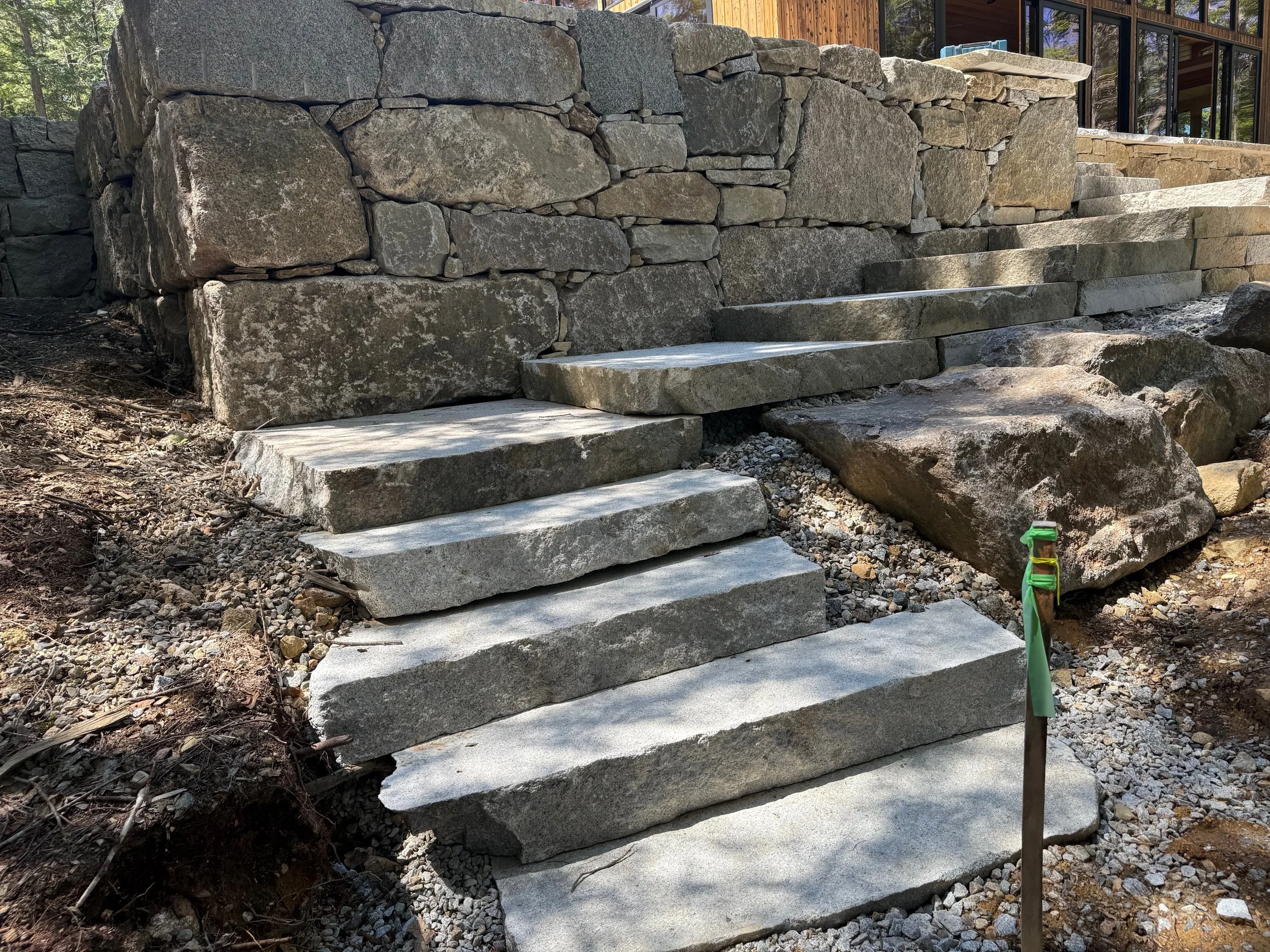 Granite staircase with large steps in garden leading up to a building and granite wall