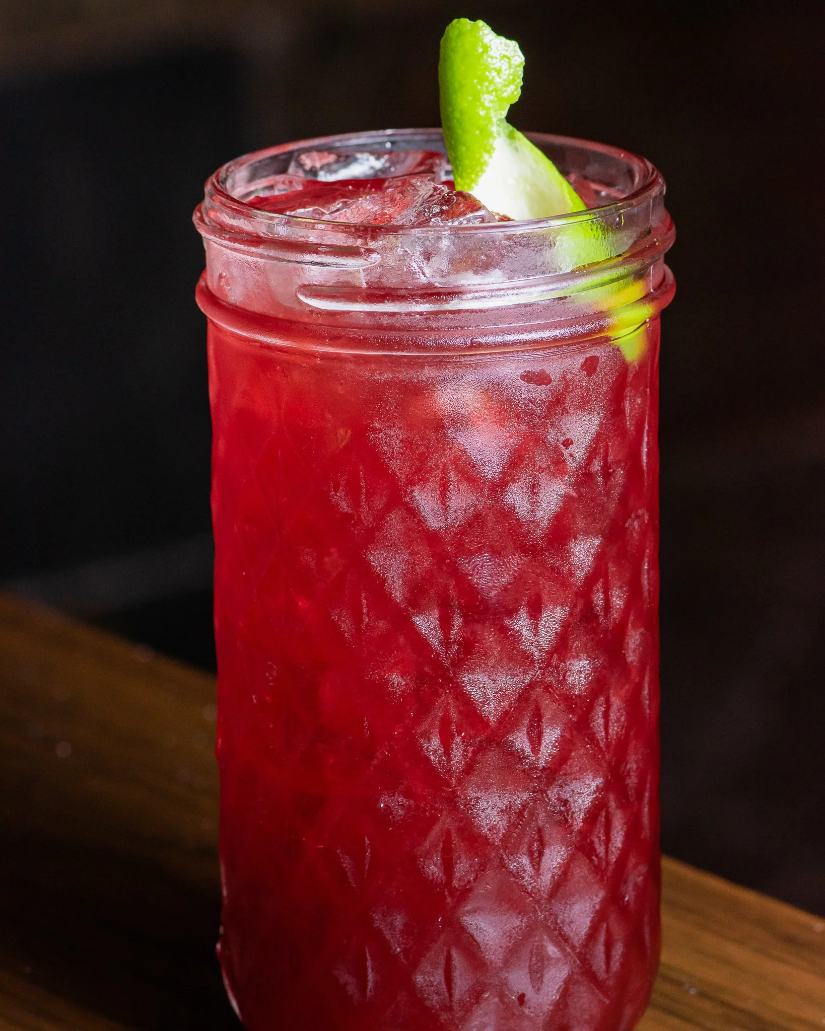 Vibrant hibiscus cocktail served in a textured glass with ice and a fresh lime zest garnish.